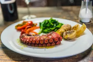 Polvo na brasa com molho à base de pimentão, em vez do azeite quente com alho, e, por isso, mais à galega do que à lagareiro