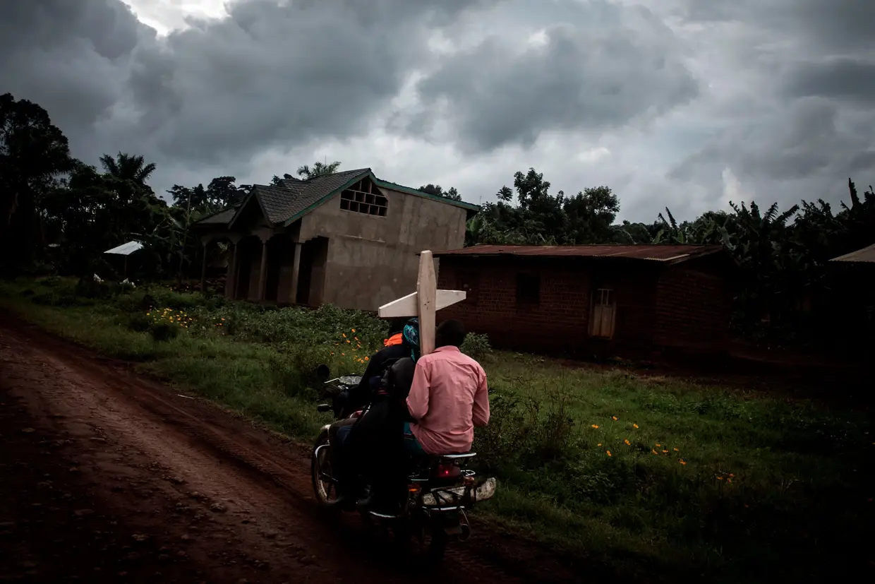 Três congoleses de moto carregam uma cruz por um túmulo ao longo da estrada que liga Mangina a Beni em 23 de agosto de 2018 em Mangina, na província de Kivu do Norte