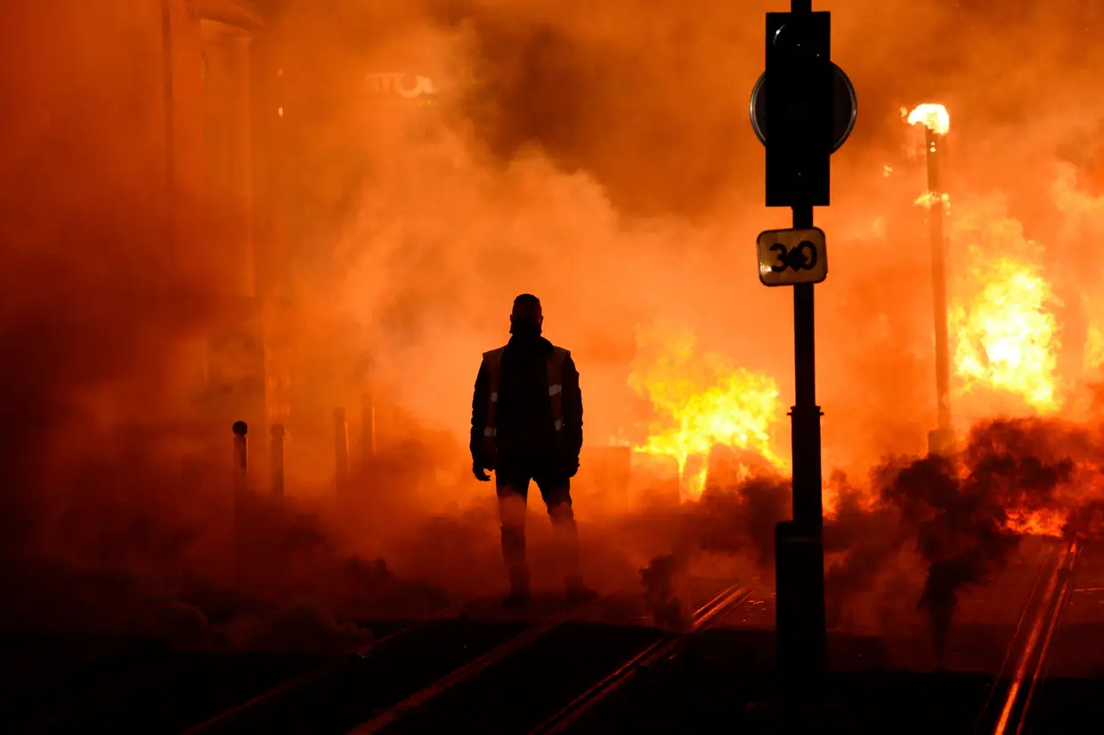 Um manifestante está perto de um incêndio em 8 de dezembro de 2018 em Bordeaux, no sudoeste da França, na linha lateral de uma manifestação contra o aumento dos custos de vida. O movimento "colete amarelo" na França começou originalmente como um protesto sobre aumentos planeados de combustível, mas transformou-se num protesto em massa contra as políticas do presidente e o estilo de governo de cima para baixo.