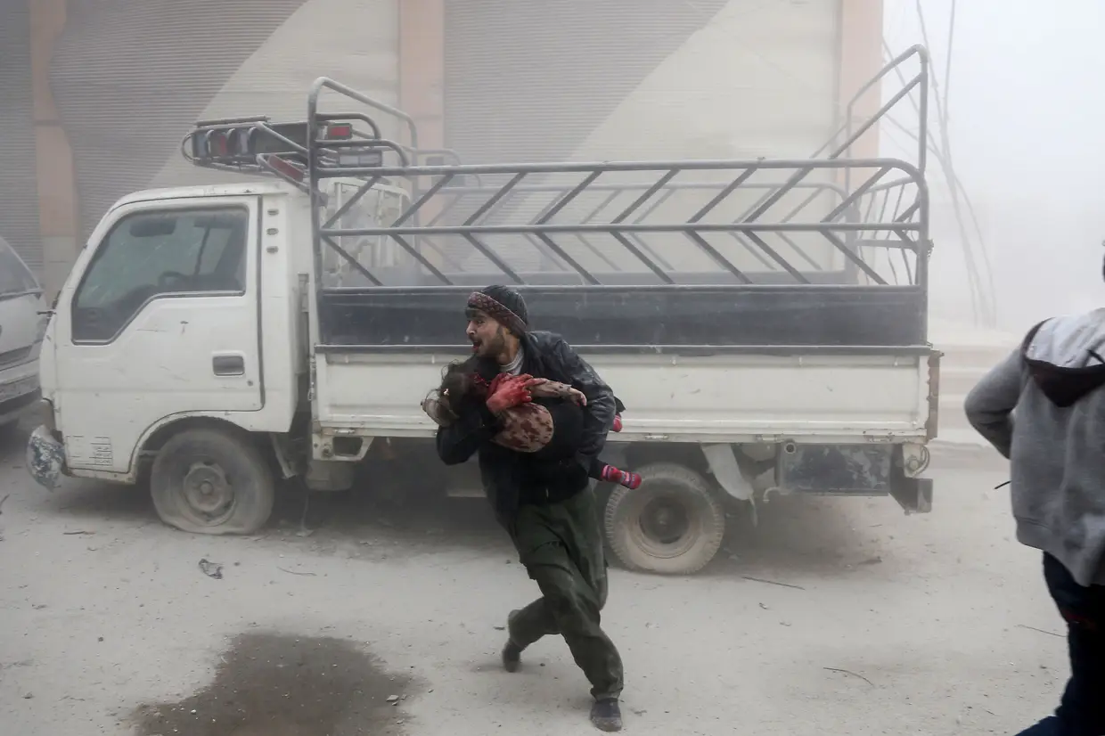 Um homem carrega uma criança enquanto foge de ataques aéreos da Síria que atingiram a cidade rebelde de Saqba, na região sitiada de Ghouta, na periferia da capital Damasco, em 6 de fevereiro de 2018