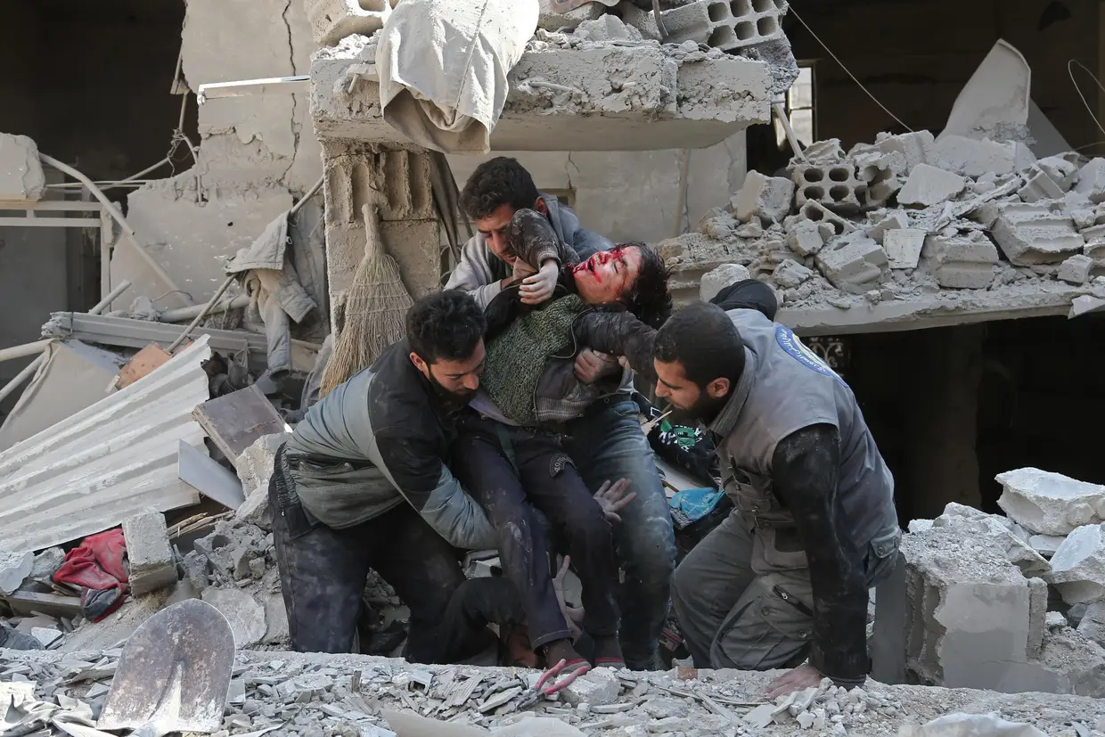 Três sírios resgatam uma criança após um ataque aéreo do regime na cidade de Hamouria, na região de Ghouta, nos arredores da capital Damasco, em 21 de fevereiro de 2018