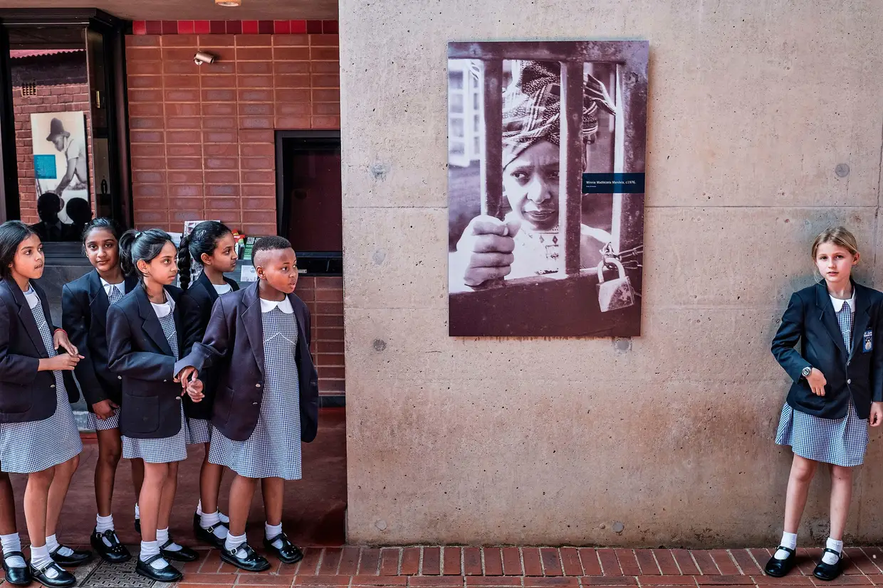 Crianças de uma escola sul-africana fazem uma pausa ao lado de um retrato da ex-ativista sul-africana anti-apartheid Winnie Madikizela-Mandela, ex-mulher do líder Nelson Mandela, em sua casa em 3 de abril de 2018, no Soweto
