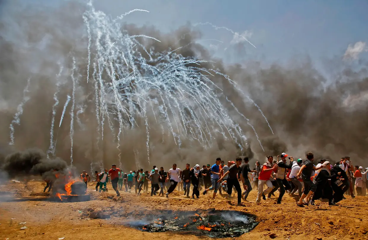 Palestinos fogem das bombas de gás lacrimogêneo durante confrontos com forças de segurança israelitas perto da fronteira entre Israel e a Faixa de Gaza, a leste de Jabalia em 14 de maio de 2018, durante os protestos contra a decisão dos EUA mudarem a sua embaixada para Jersualém