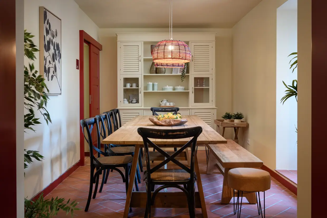 A sala de refeições, com uma mesa comunitária, e ao fundo a pequena cozinha, totalmente equipada