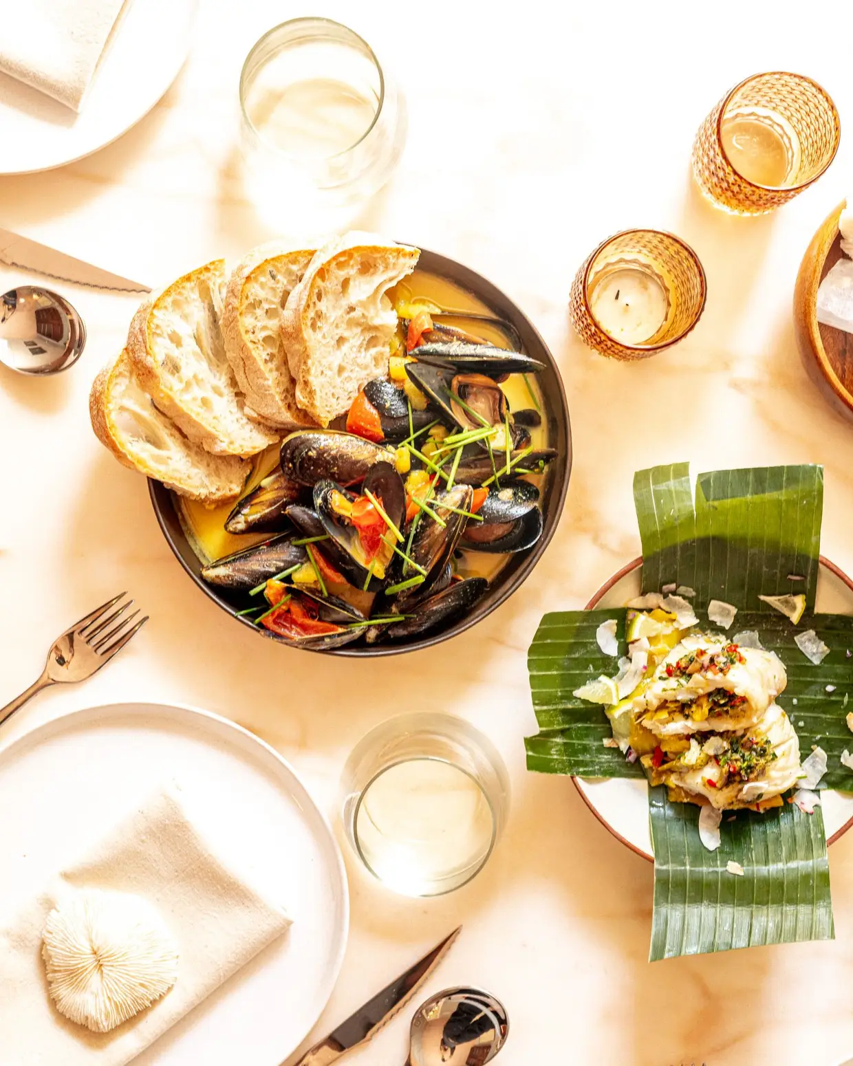 Oeixe branco envolvido em folha de bananeira, com ervas asiáticas, leite de coco e manga, e mexilhões à moda Thai, servidos em caril com pão local