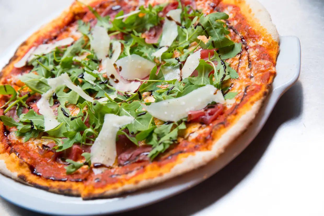 A pizza Carpaccio leva tomate esmagado com carne de vaca, mozzarella, parmesão ralado, rúcula e redução balsâmica doce