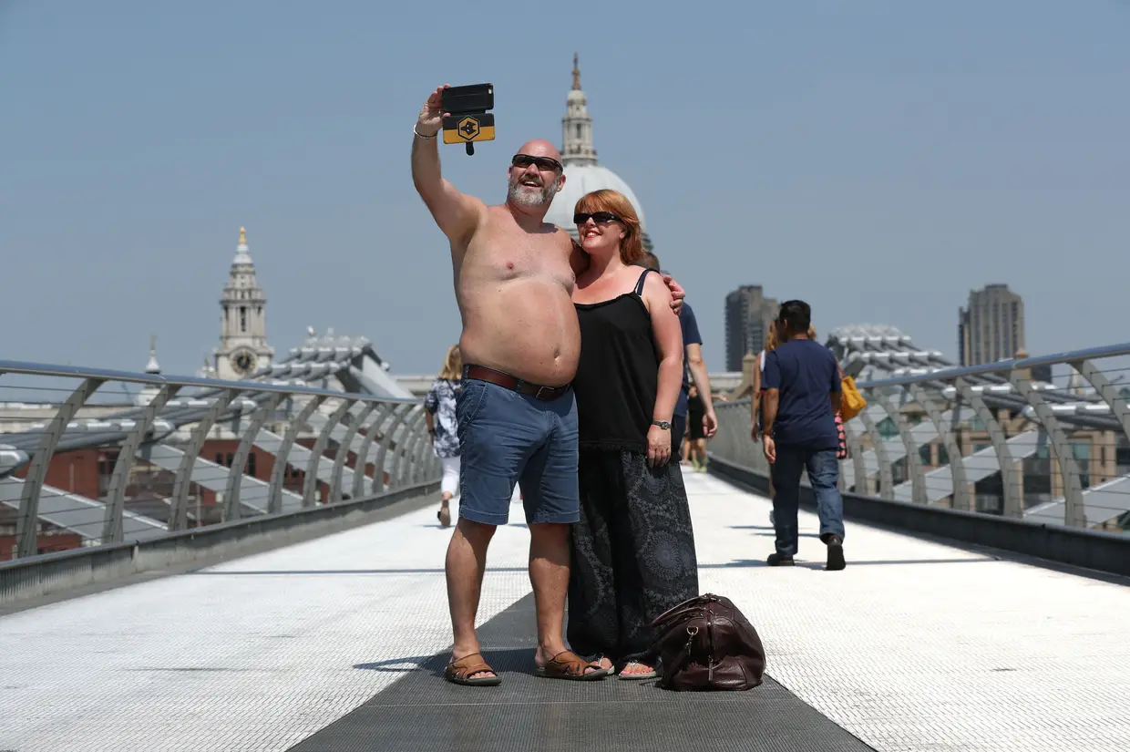 Casal de turistas em traje de praia tiram uma “selfie” sobre a Ponte do Milénio, em Londres, Reino Unido