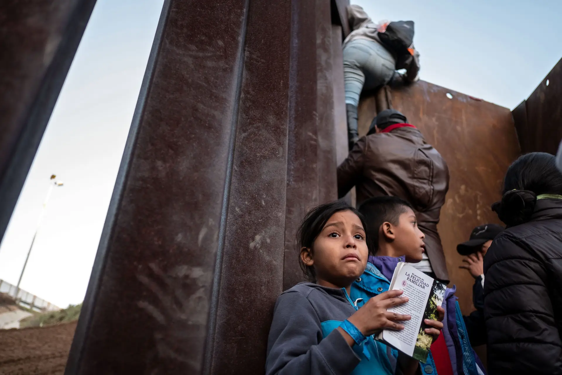 Crianças integradas na caravana de migrantes esperam por vez para trepar a vedação que serve de fronteira entre o México e os EUA, na zona de Tijuana