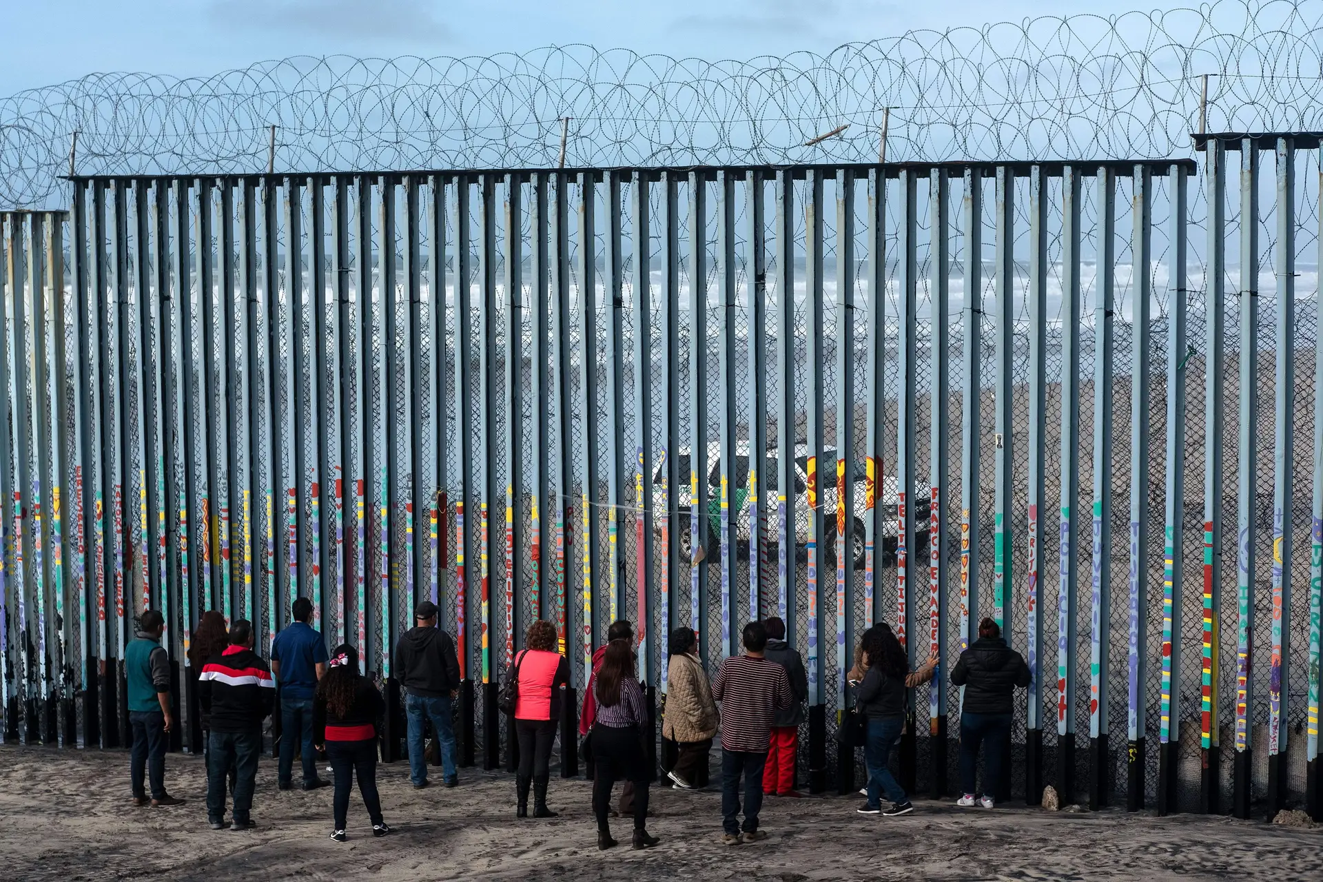 Migrantes junto ao muro na fronteira entre o México e os EUA