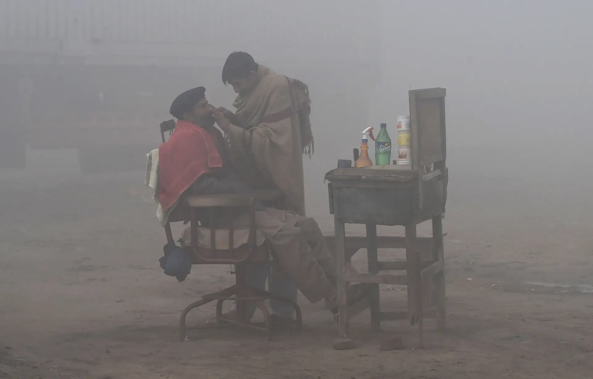 PAQUISTÃO. Por detrás de uma “tela” de poluição, um barbeiro atende um cliente, numa rua de Lahore