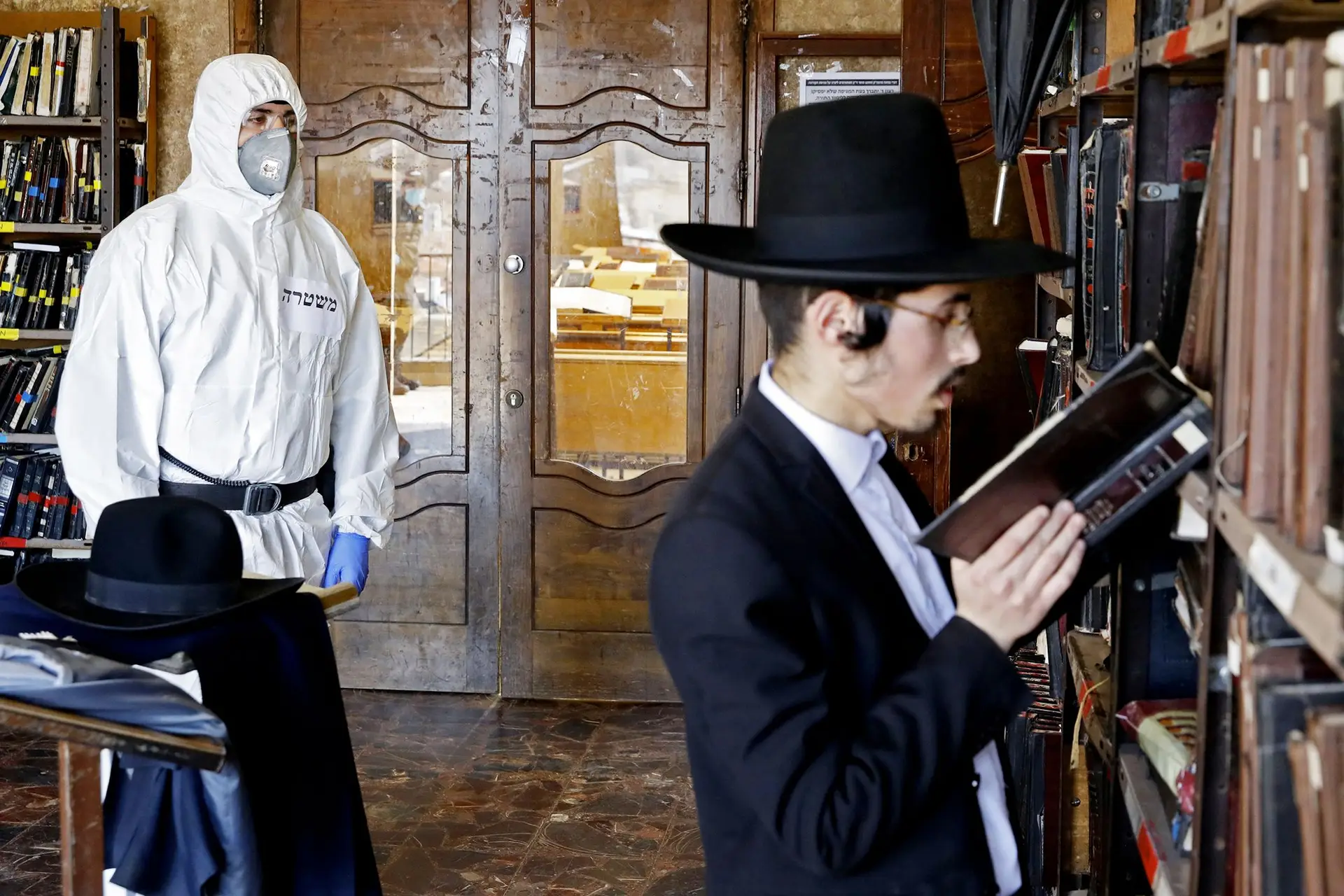 No interior de uma “yeshiva”, na cidade de Bnei Brak, um ultraortodoxo, entregue ao estudo, ignora o polícia equipado com fato protetor