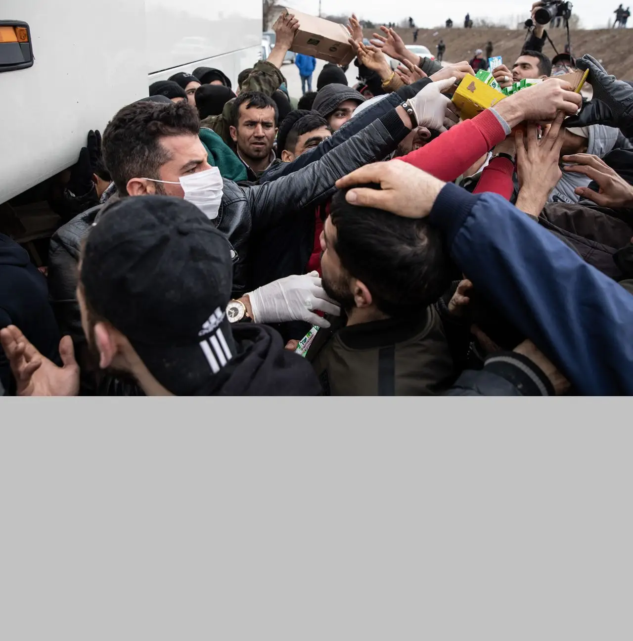 Um voluntário de uma ONG, protegido com uma máscara respiratória, distribui comida a refugiados e migrantes na fronteira entre a Turquia e a Grécia