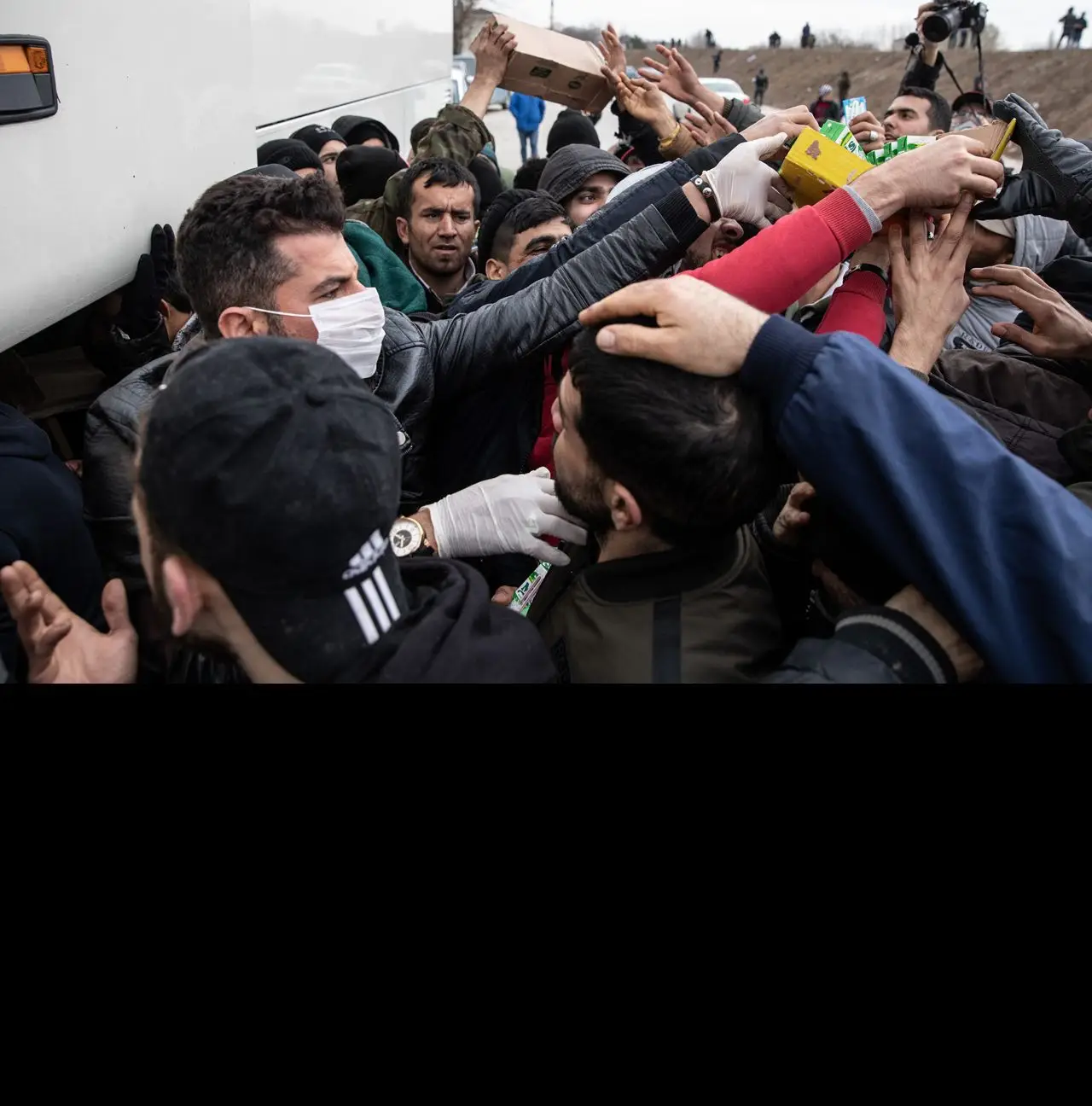 Um voluntário de uma ONG, protegido com uma máscara respiratória, distribui comida a refugiados e migrantes na fronteira entre a Turquia e a Grécia