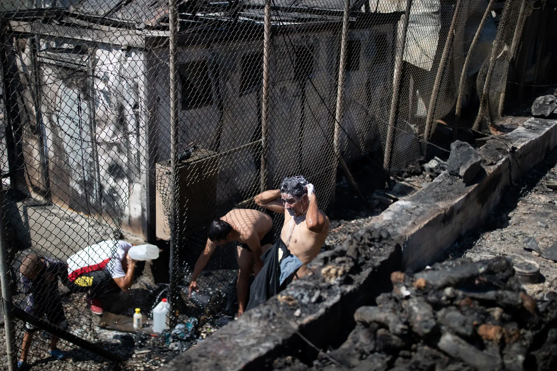 Habitantes do campo de Moria lavam-se junto aos abrigos destruídos pelas chamas