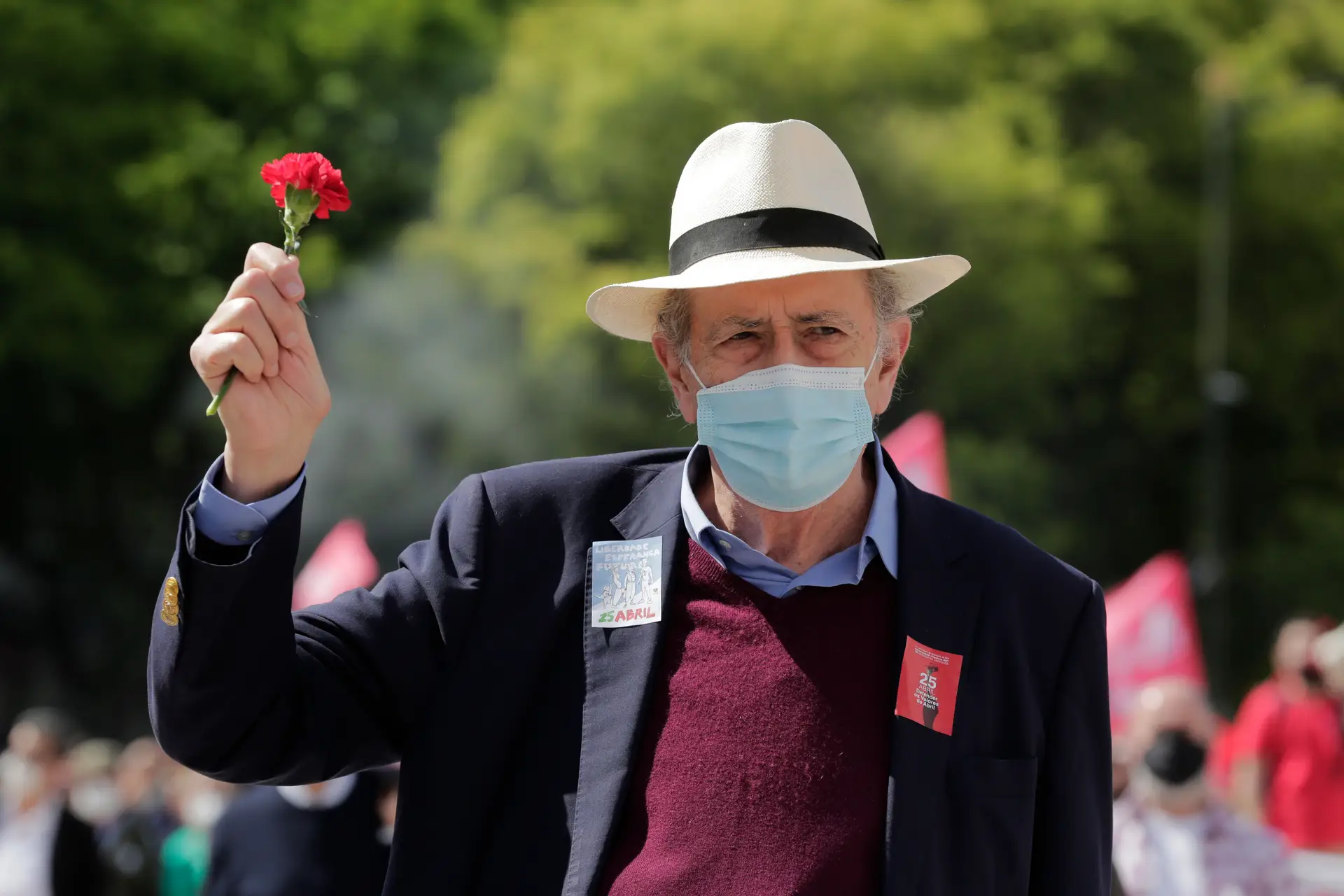 O realizador António-Pedro Vasconcelos com a cara coberta pela máscara e a cabeça coberta pelo chapéu, empunhando um cravo vermelho em nome do pensamento livre que Abril não deixa confinar