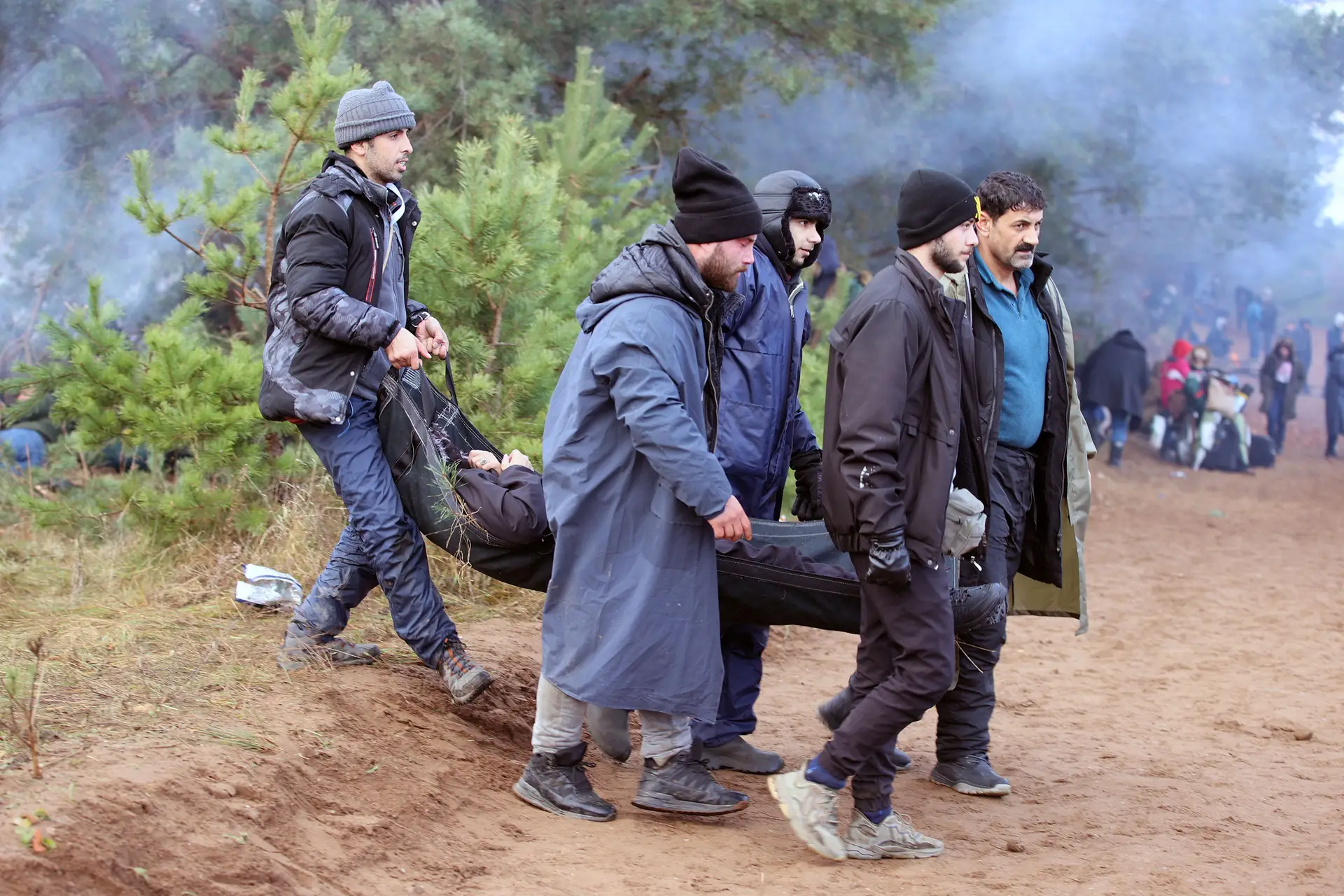 Migrantes carregam pessoa em maca para ajuntamento na fronteira da Bielorrússia com a Polónia
