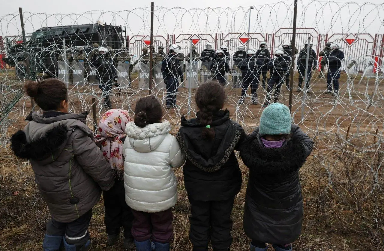 Crianças, junto à vedação em arame que funciona como fronteira, observam agentes de segurança polacos destacados para a fronteira com a Bielorrússia