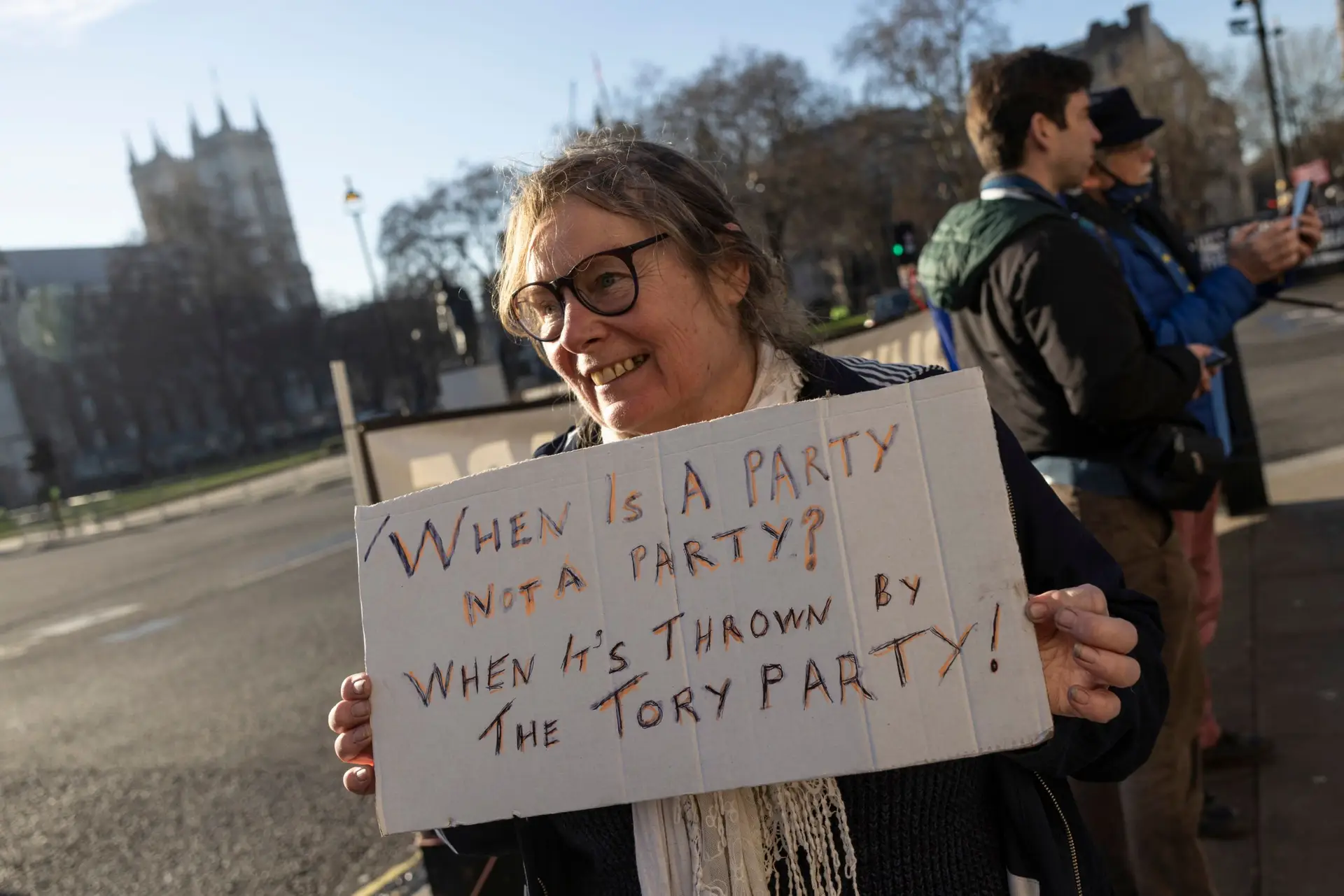 Manifestante diante do Parlamento britânico com um cartaz onde se lê: “Quando é que uma festa não é uma festa? Quando é organizada pelo Partido Conservador” (FOTO Dan Kitwood/Getty Images)