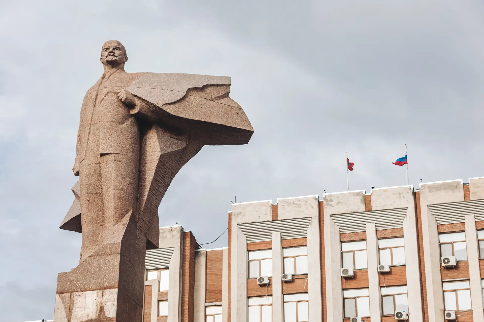 Estátua de Lenine em frente ao Palácio Presidencial de Tiraspol, a capital da Transnístria. No topo estão hasteadas as bandeiras do autoproclamado Estado independente de Transnístria e da Rússia