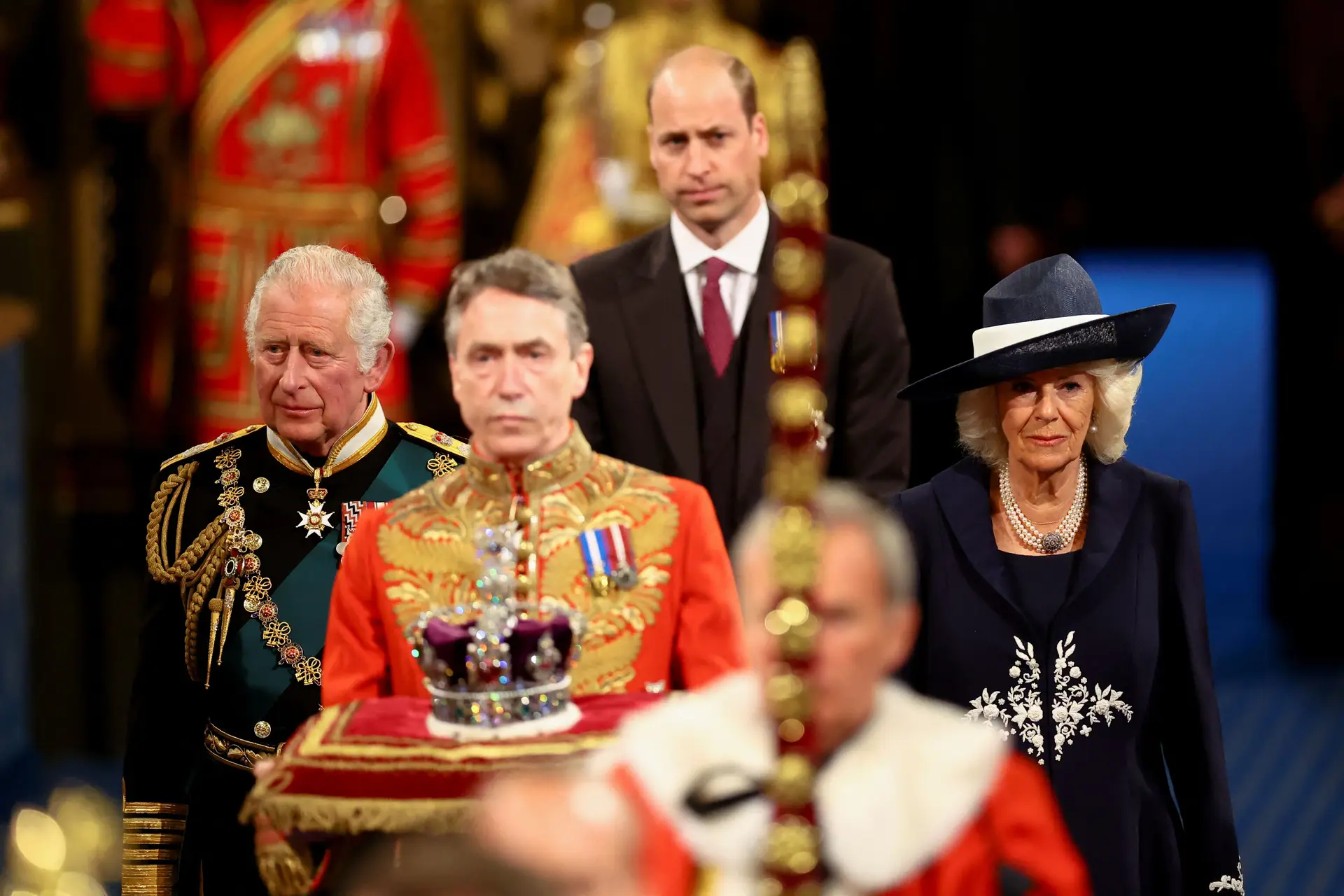 Coube a Carlos, príncipe de Gales (acompanhado na imagem da mulher, Camilla, e do filho William), ler o discurso escrito pelo Governo, por a rainha estar a sofrer de dores de costas que lhe limitam a mobilidade. A coroa tarnsportada à frente do herdeiro representa a monarca ausente