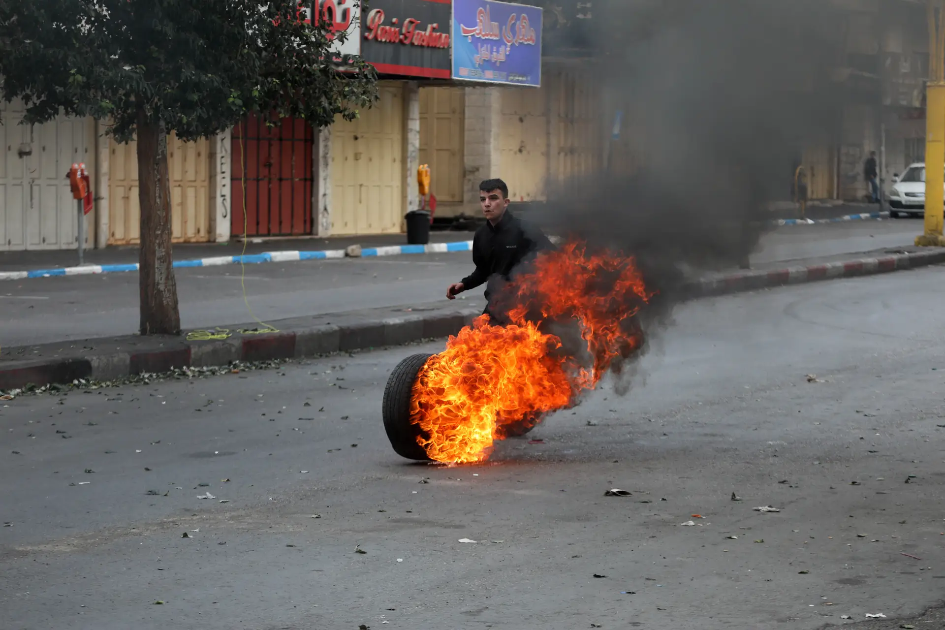 Um palestiniano arremessa um pneu em chamas na direção de um ‘checkpoint’ militar israelita, na cidade de Hebron (Cisjordânia)
