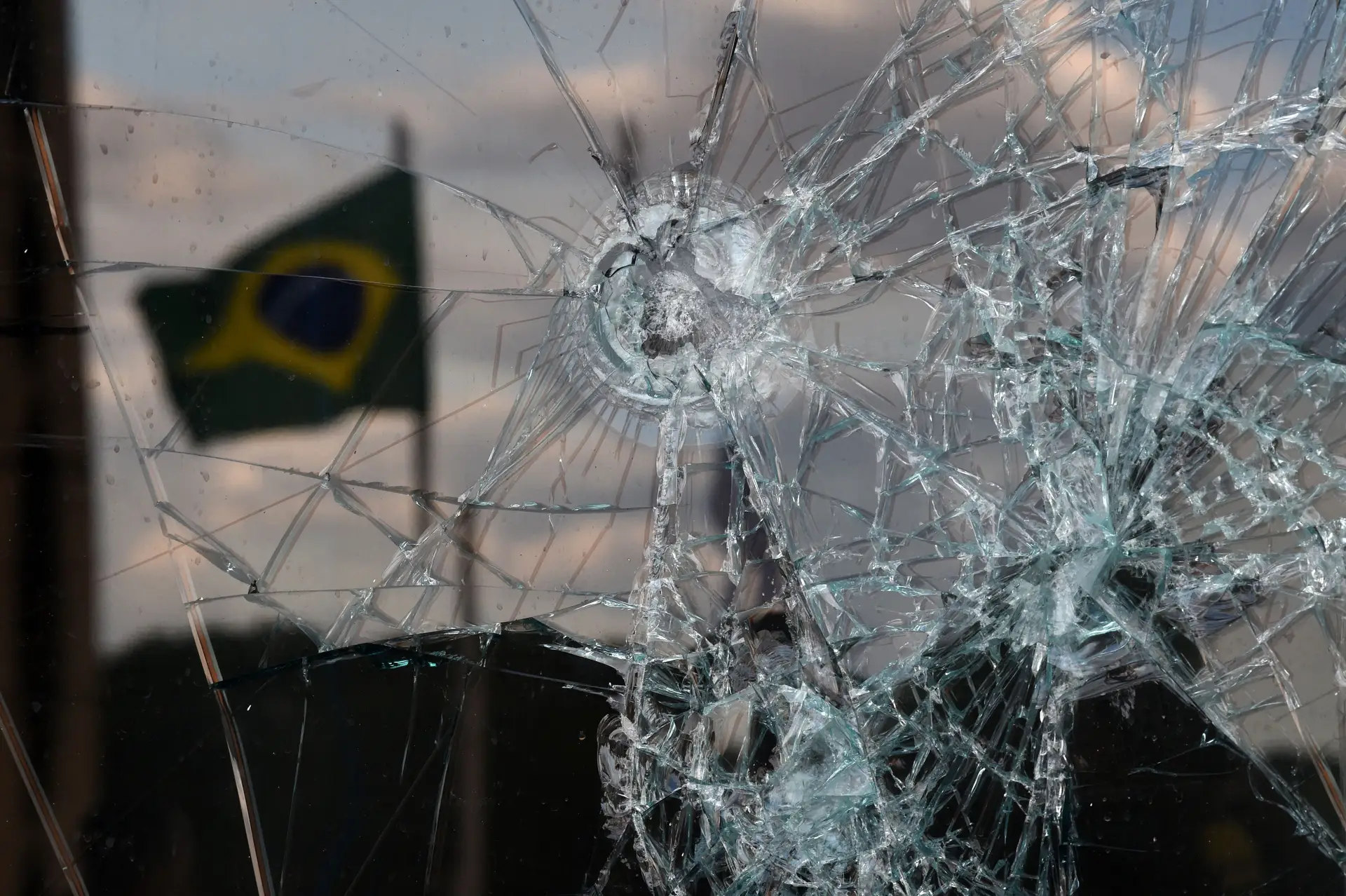 O reflexo de uma bandeira brasileira num vidro do edifício do Supremo Tribunal, estilhaçado pelos invasores