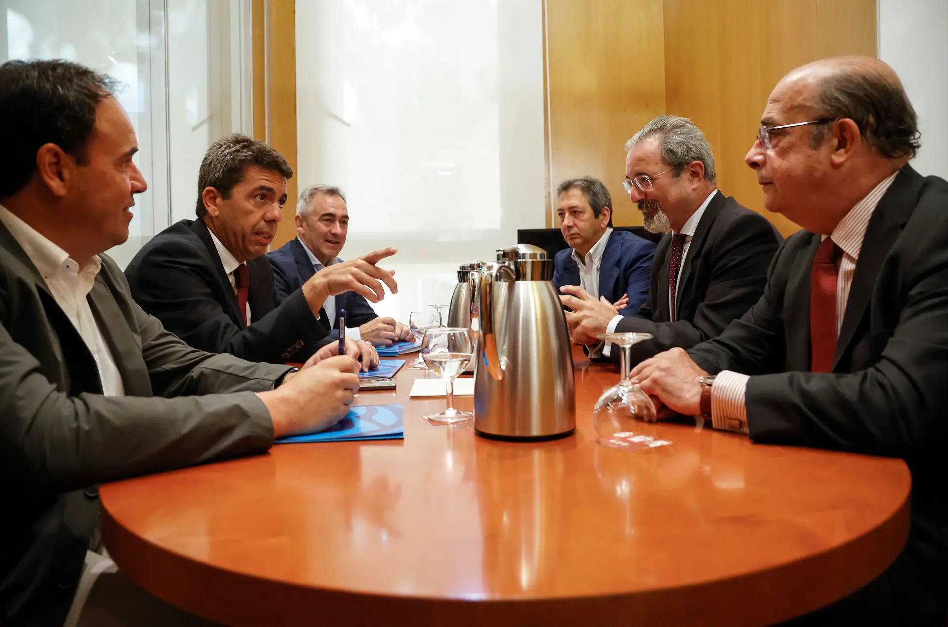 Negociações entre PP e Vox em Valência. À esquerda, de mão no ar, Carlos Mazón, novo presidente da região; à sua frente, de óculos e barba, Carlos Flores, do Vox, agressor condenado por violência doméstica  