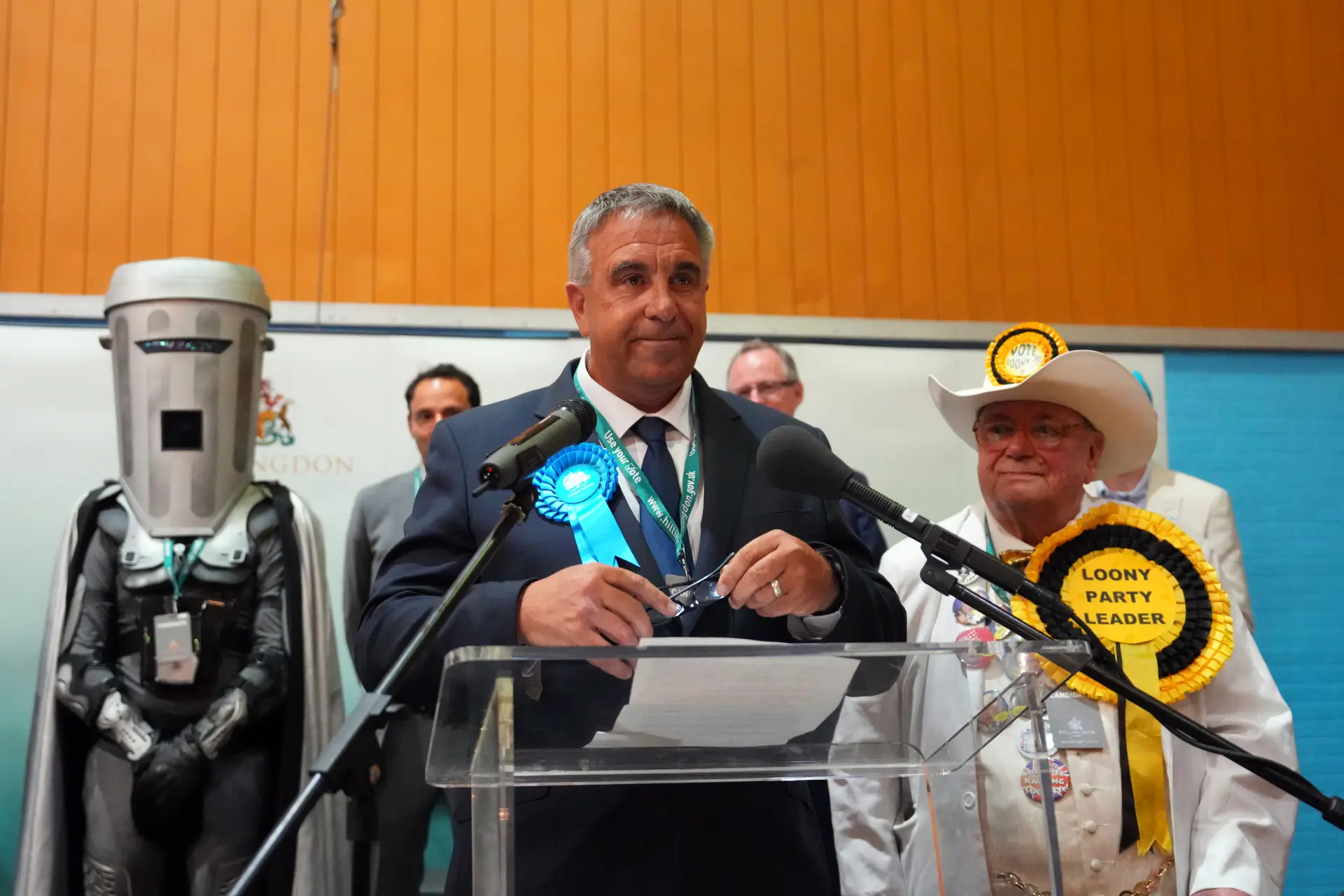 O conervador Steve Tuckwell celebra a vitória em Uxbridge e Ruislip Sul, ladeado pelos candidatos satíricos Conde Cara de Caixote (independente) e Howling Laud Hope, do Partido Oficial dos Monstros Malucos das Festas