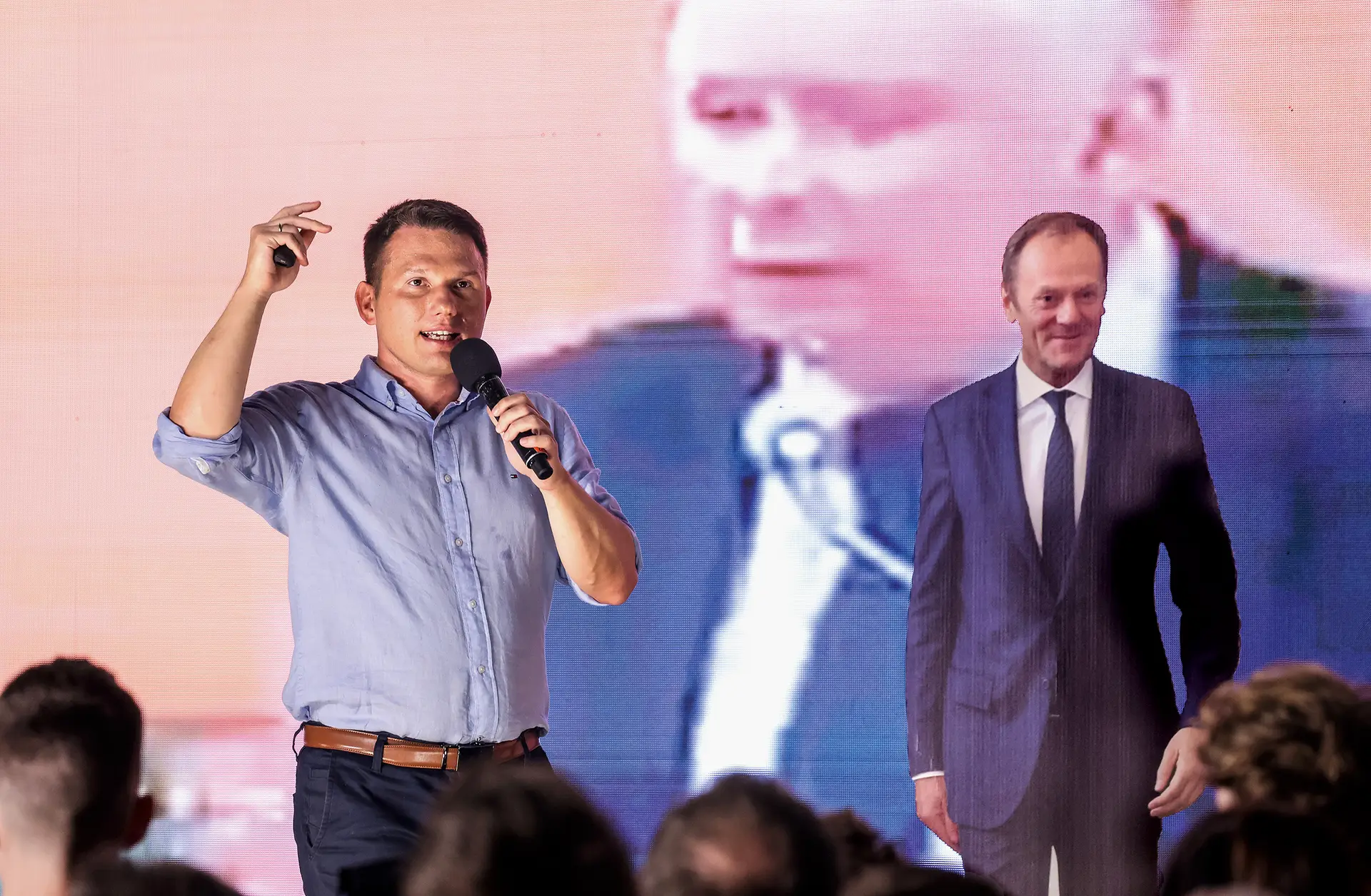 Slawomir Mentzen intervém num comício da KWN (extrema-direita) para equiparar o ultraconservador Jaroslaw Kaczynski (na imagem de fundo) ao centrista Donald Tusk