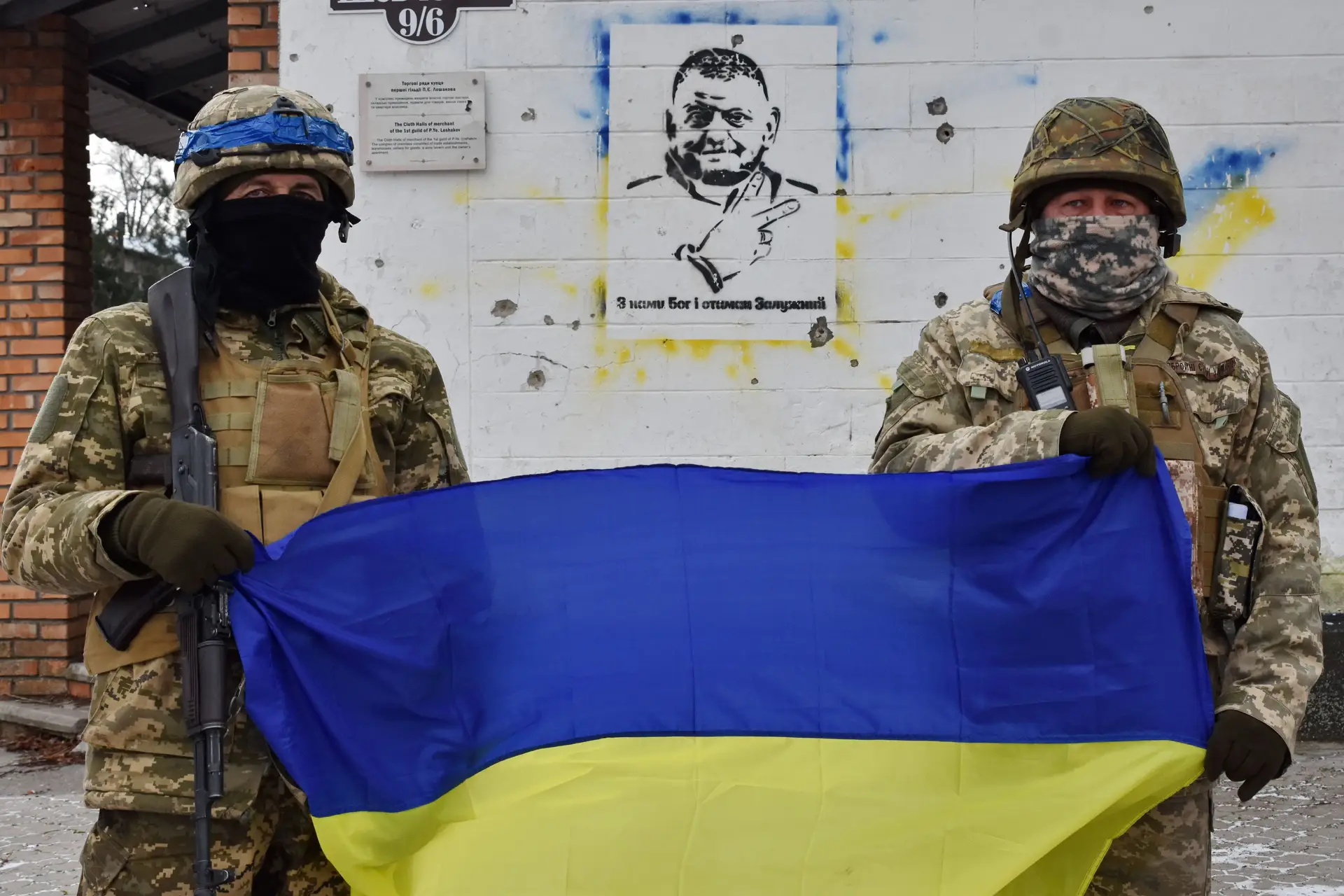 Soldados ucranianos com a bandeira nacional, diante de um grafito com a imagem do general Valery Zaluzhny, chefe das forças armadas do país invadido