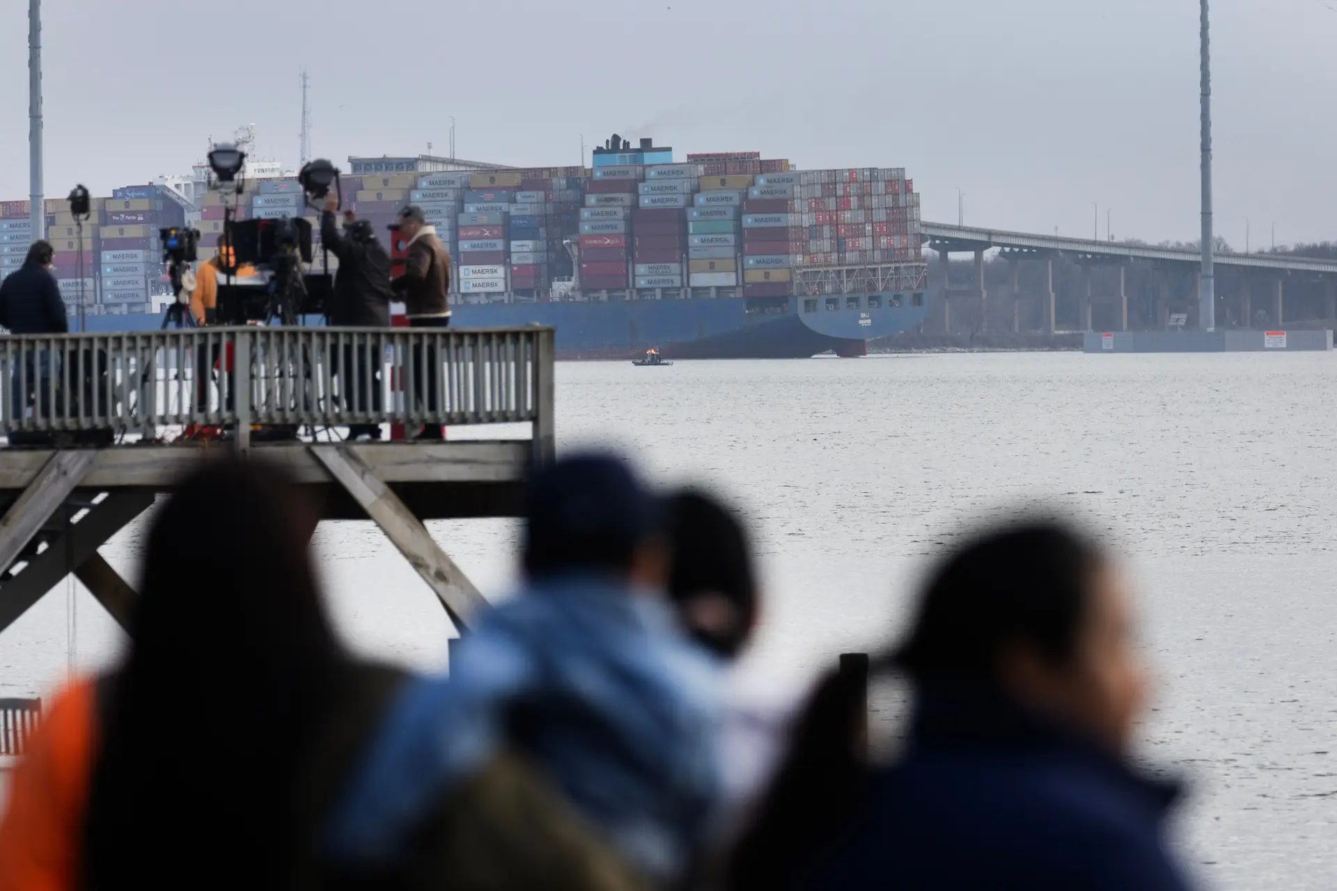 Equipas de reportagem e transeuntes reúnem-se ao longo da costa para ver o navio cargueiro que embateu e fez ruir a ponte Francis Scott Key, em Baltimore, nos Estados Unidos.