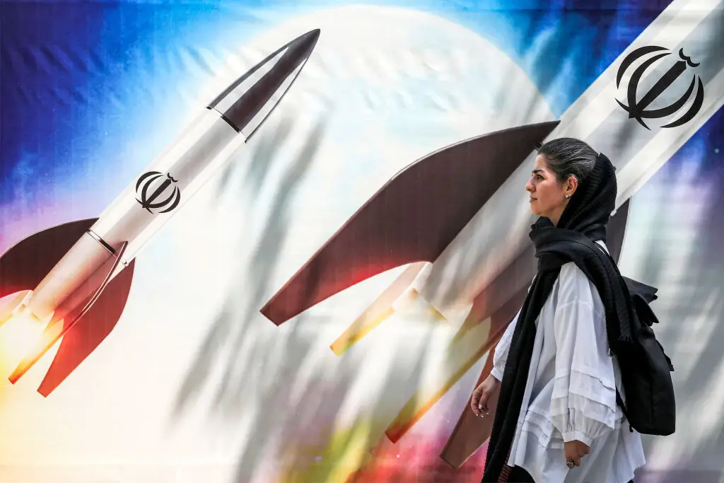 Em Teerão, uma iraniana passa junto a um mural de mísseis com o símbolo da República Islâmica