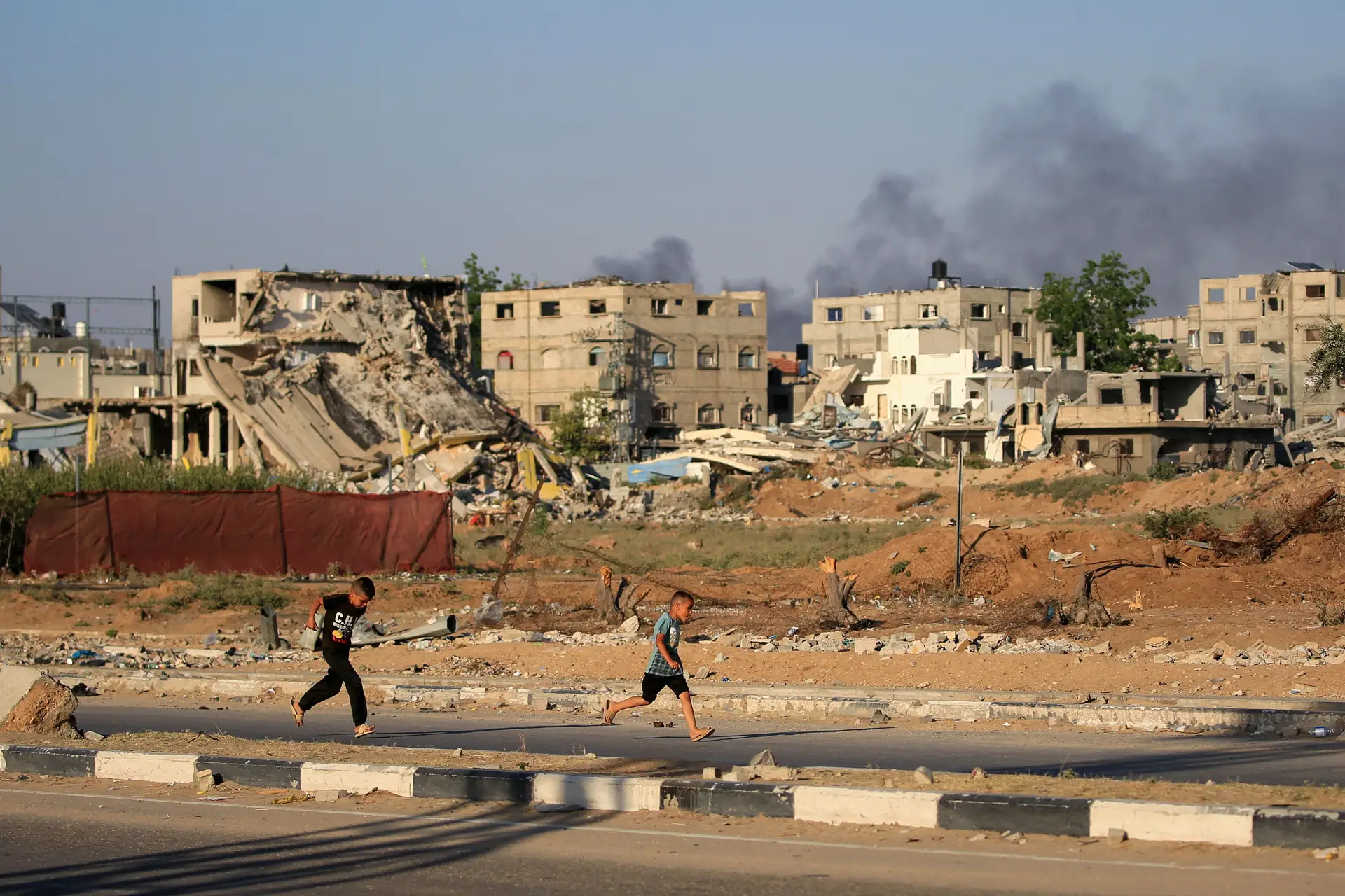 Rapazes palestinianos correm enquanto o fumo se espalha durante um bombardeamento israelita a leste do campo de refugiados de al-Bureij, no centro da Faixa de Gaza