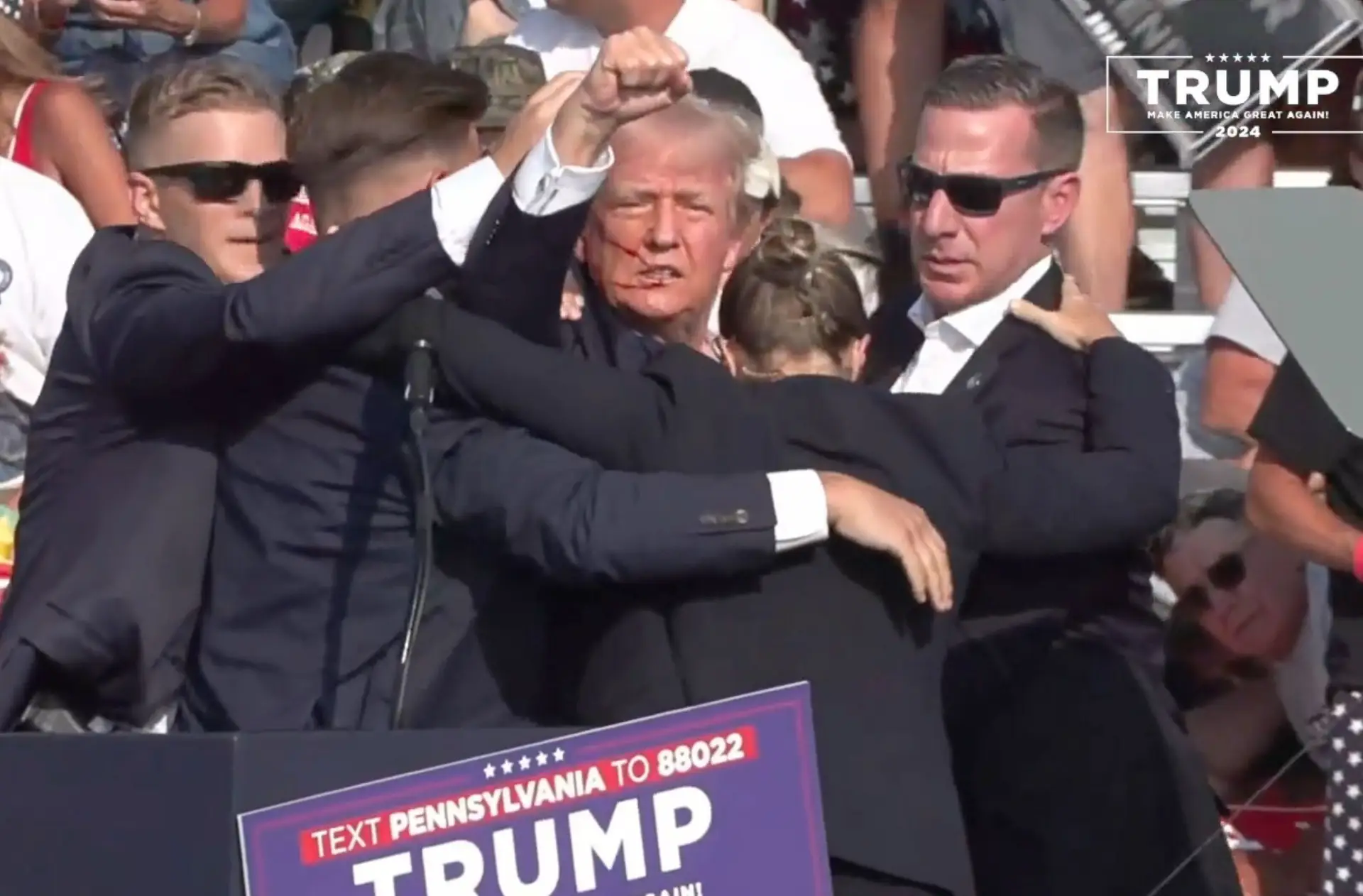 Trump, com ferimentos no rosto, é apoiado por seguranças depois de terem sido disparados feridos num comício seu