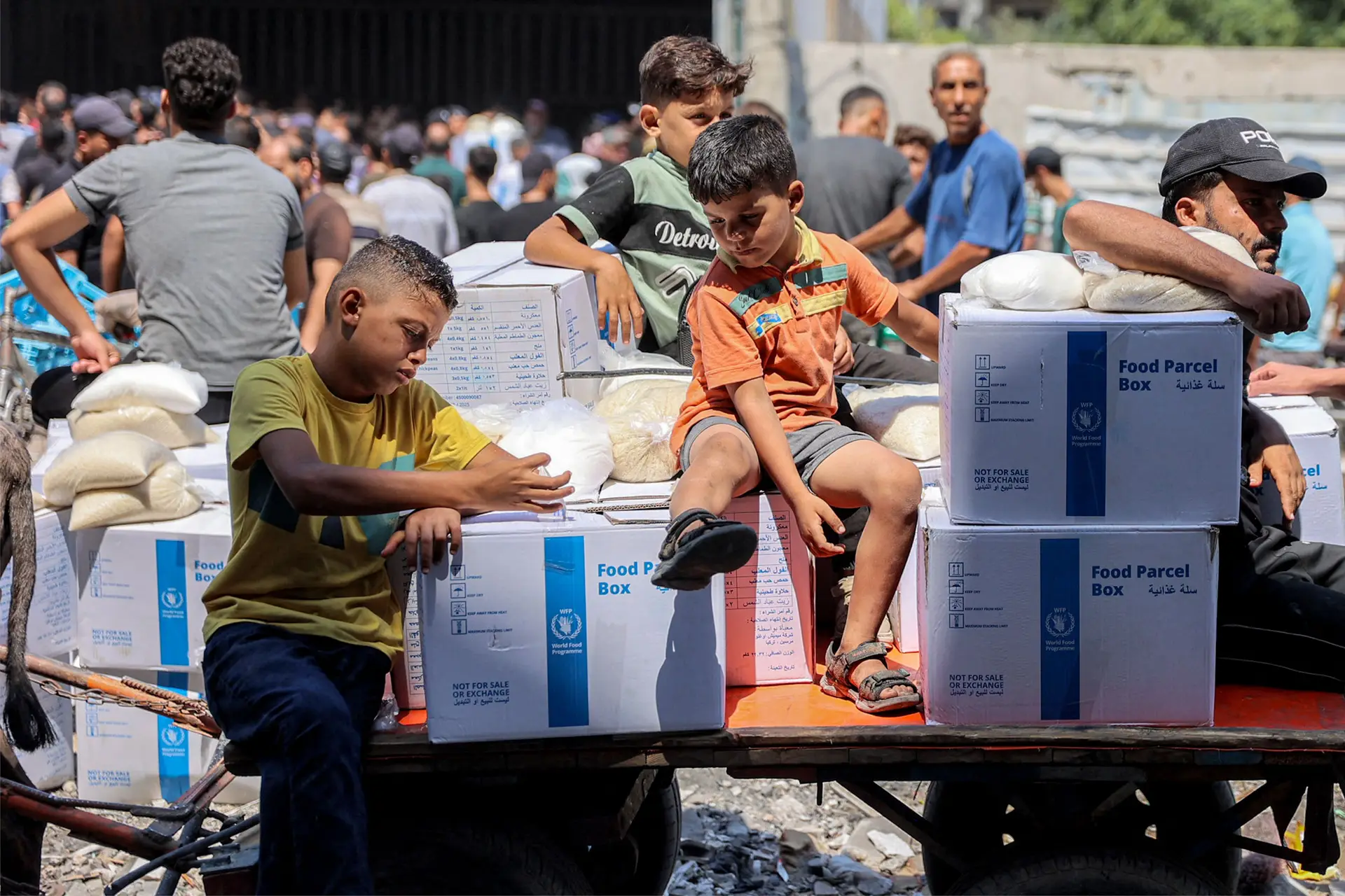 Crianças sentadas num carrinho com pacotes de ajuda humanitária da ONU