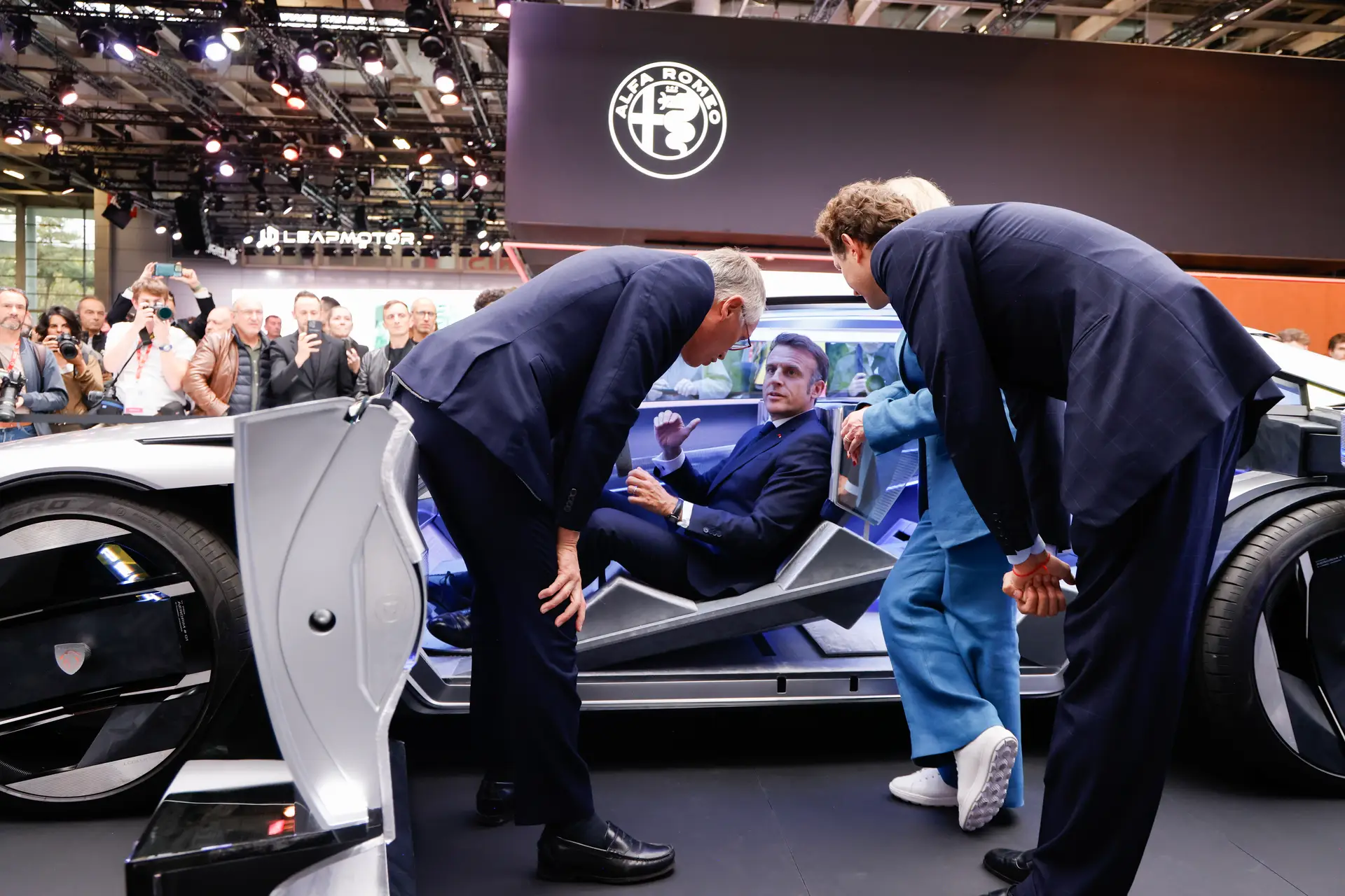 Emmanuel Macron, sentado aos comandos de um protótipo da Peugeot, enquanto fala com Carlos Tavares, presidente do grupo Stellantis (que integra 14 marcas incluindo a Peugeot)