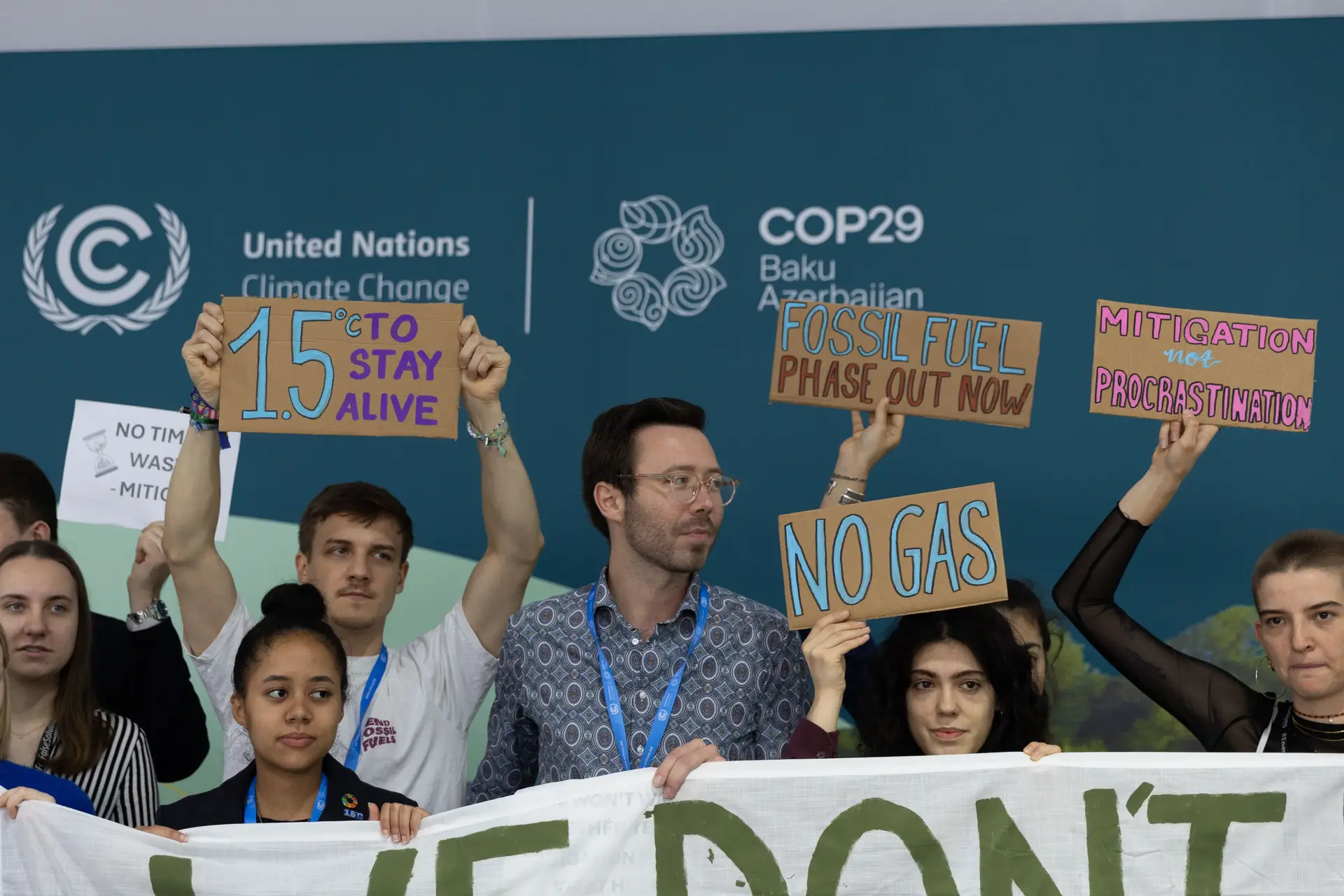 Grupo manifesta-se em silêncio nos corredores da COP29, em Baku. Erguem cartazes em que lembram que é preciso acabar com os combustíveis fósseis já para manter a meta 1,5°C