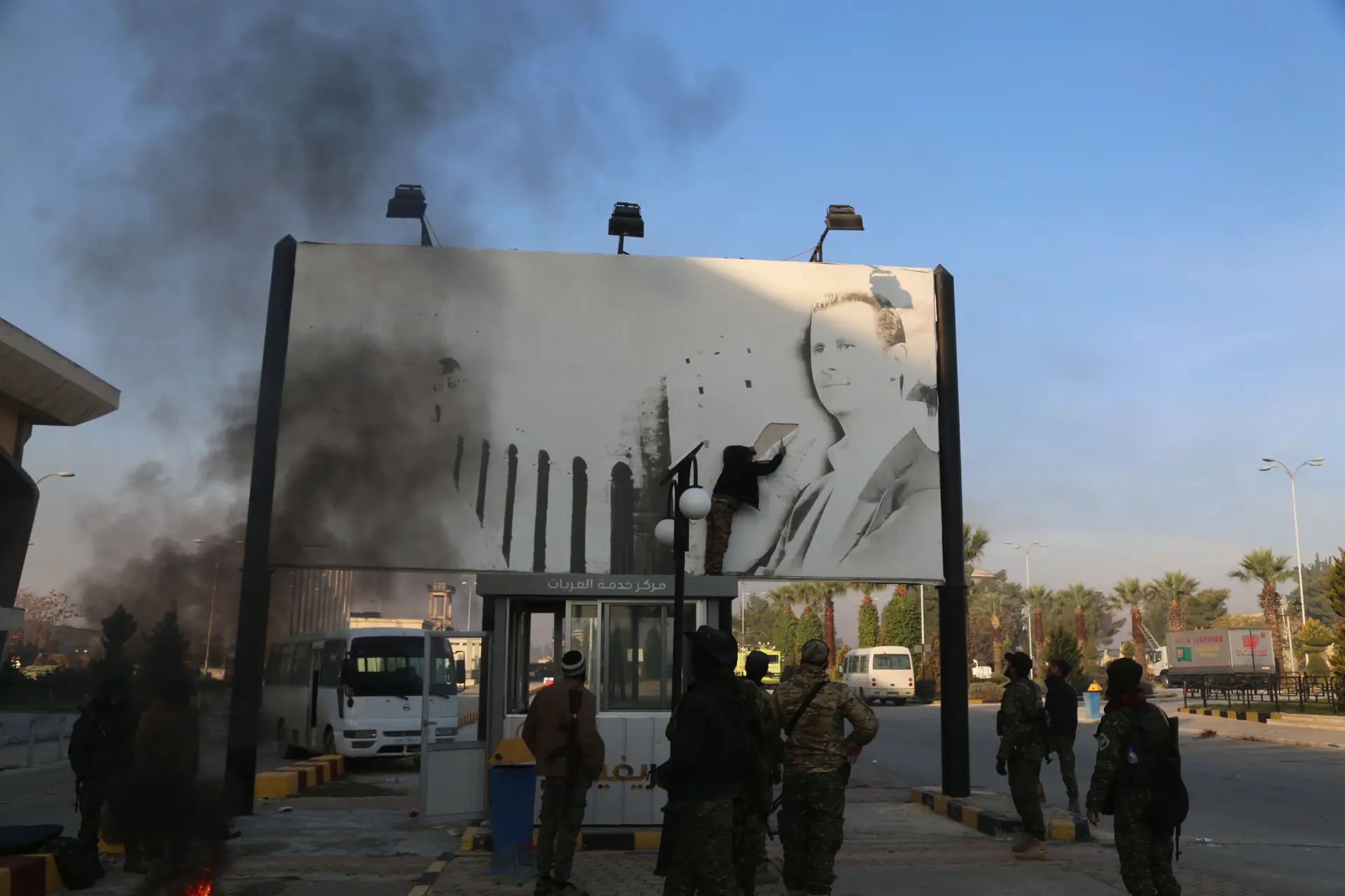 Rebeldes tentam rasgar um cartaz com a cara do Presidente Assad, perto do aeroporto internacional de Idlib, controlado pelos rebeldes no início de dezembro de 2024