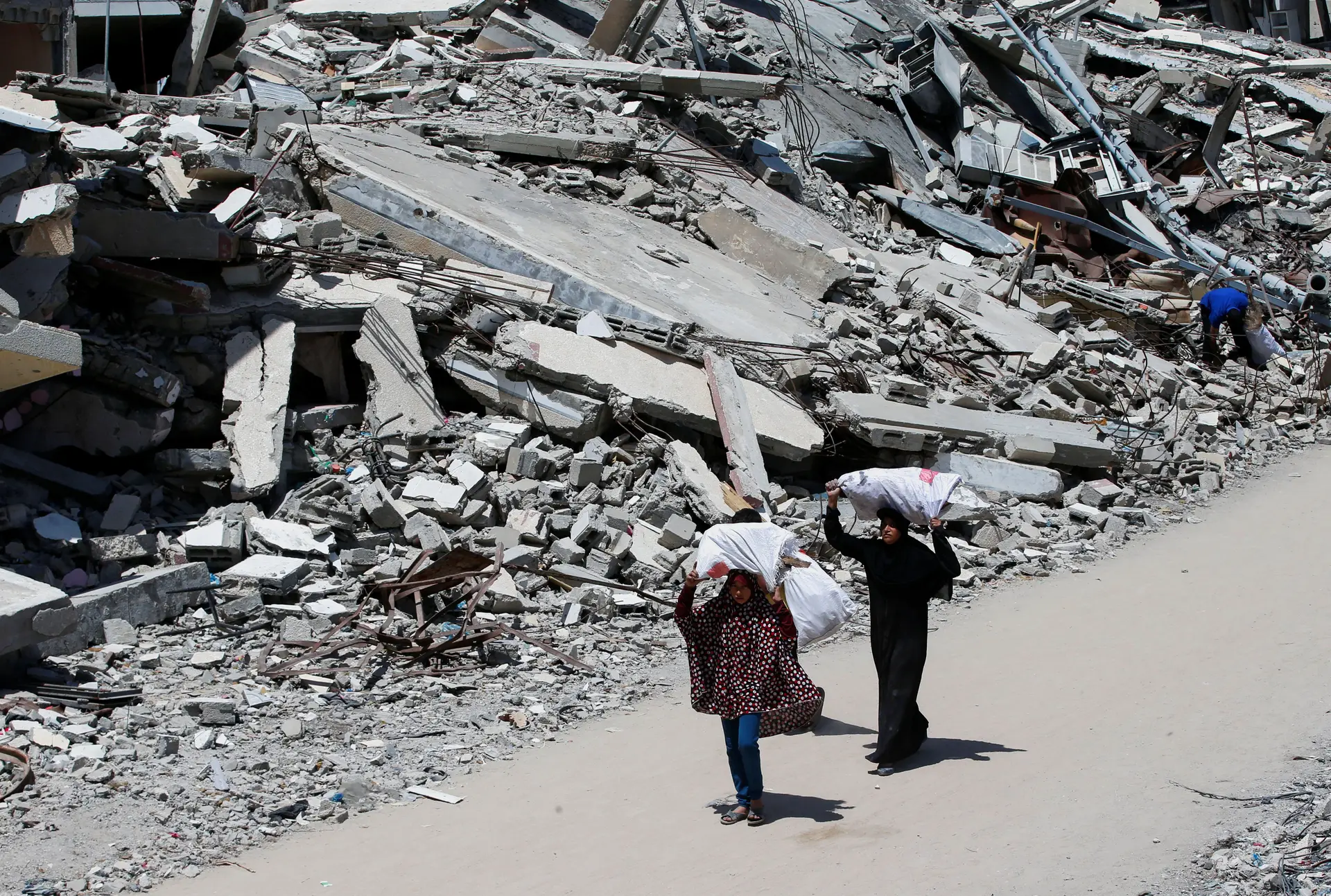 Duas palestinianas carregam sacos com lenha, entre a destruição da Cidade de Gaza