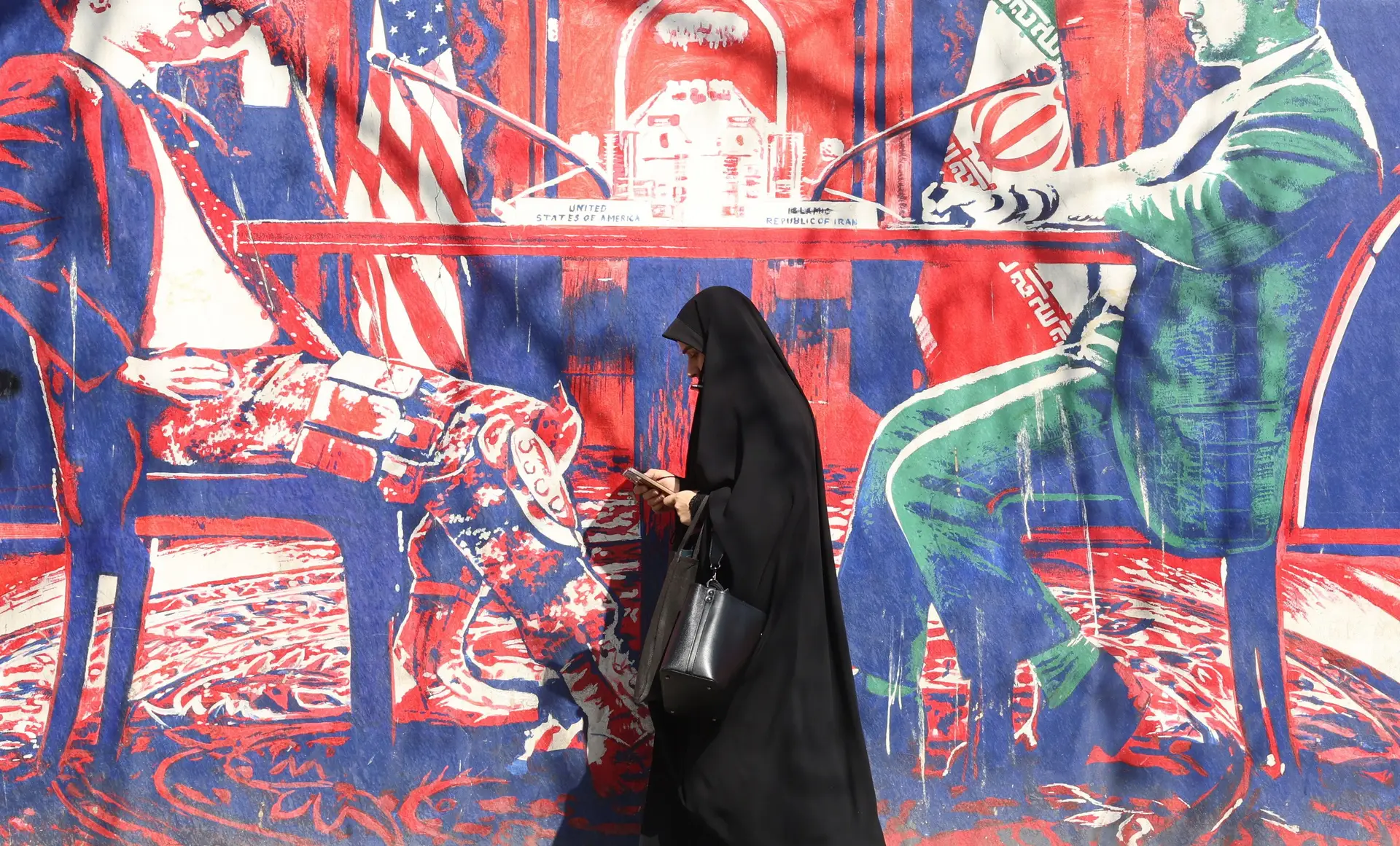 Iraniana passa junto a um mural que alude ao diálogo entre Irão e EUA, em Teerão