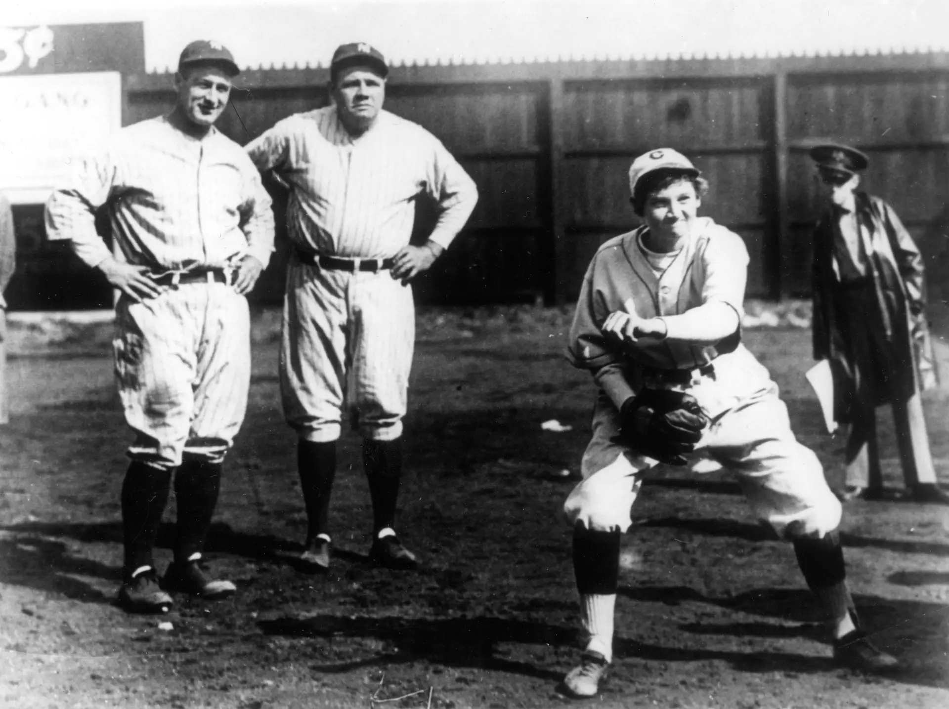 Babe Ruth, à esquerda e ao lado de Lou Gehrig, dois dos melhores batedores de sempre da história do beisebol, a observarem Jackie Mitchell a lançar.