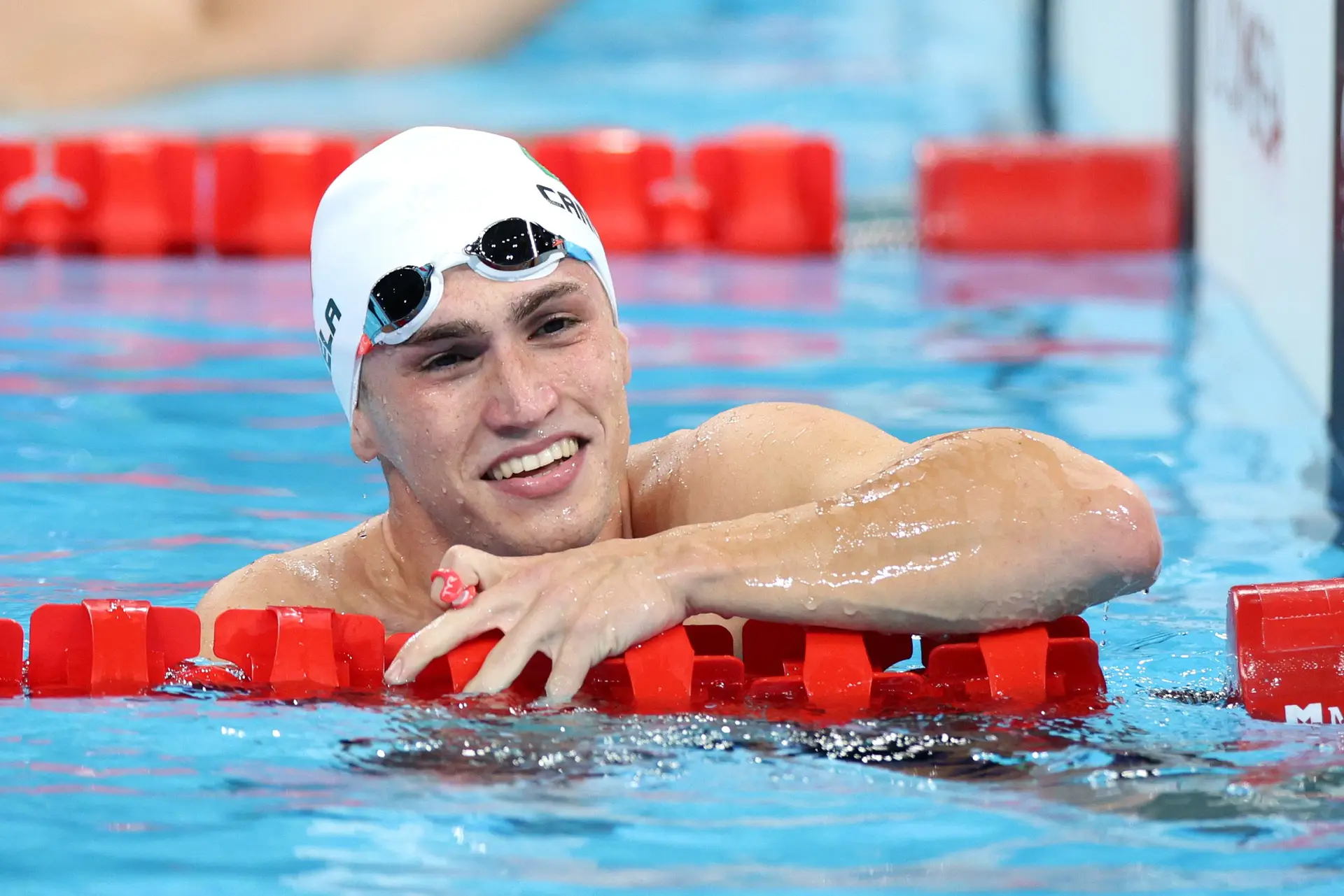 Diogo Cancela, com um grande sorriso ainda dentro de água, na piscina, com a touca branca e os óculos na cabeça.