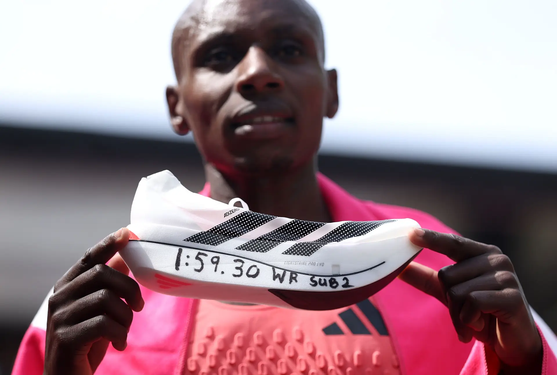 Sabastian Sawe no final da Maratona de Londres a mostrar a sapatilha da Adidas, a mais leve de sempre, com que se tornou o primeiro humano a correr a distância em menos de duas horas: e com a qual quase dividiu o protagonismo