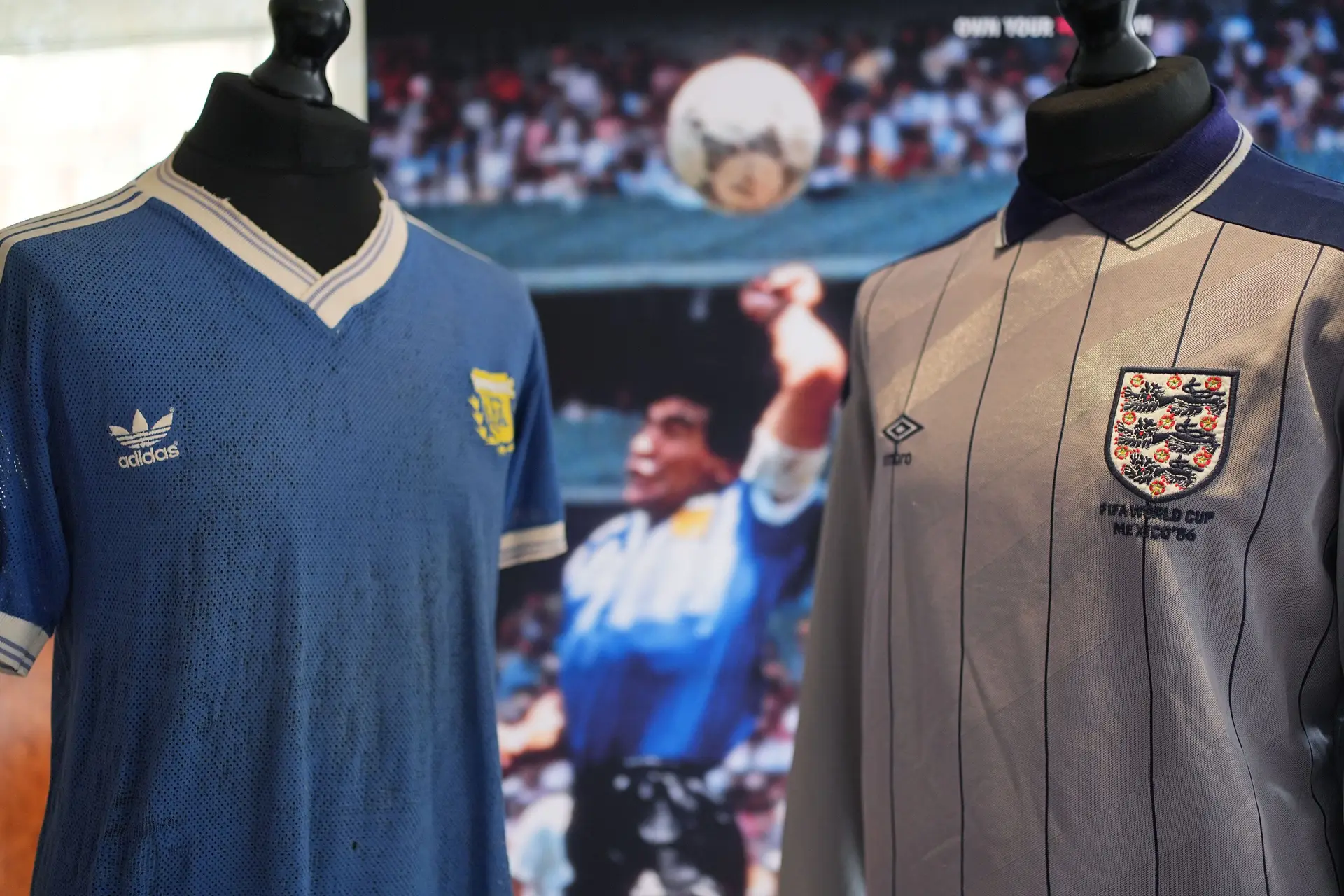 Camisolas da Argentina e de Inglaterra e, atrás, o golo de Maradona com a mão em 1986