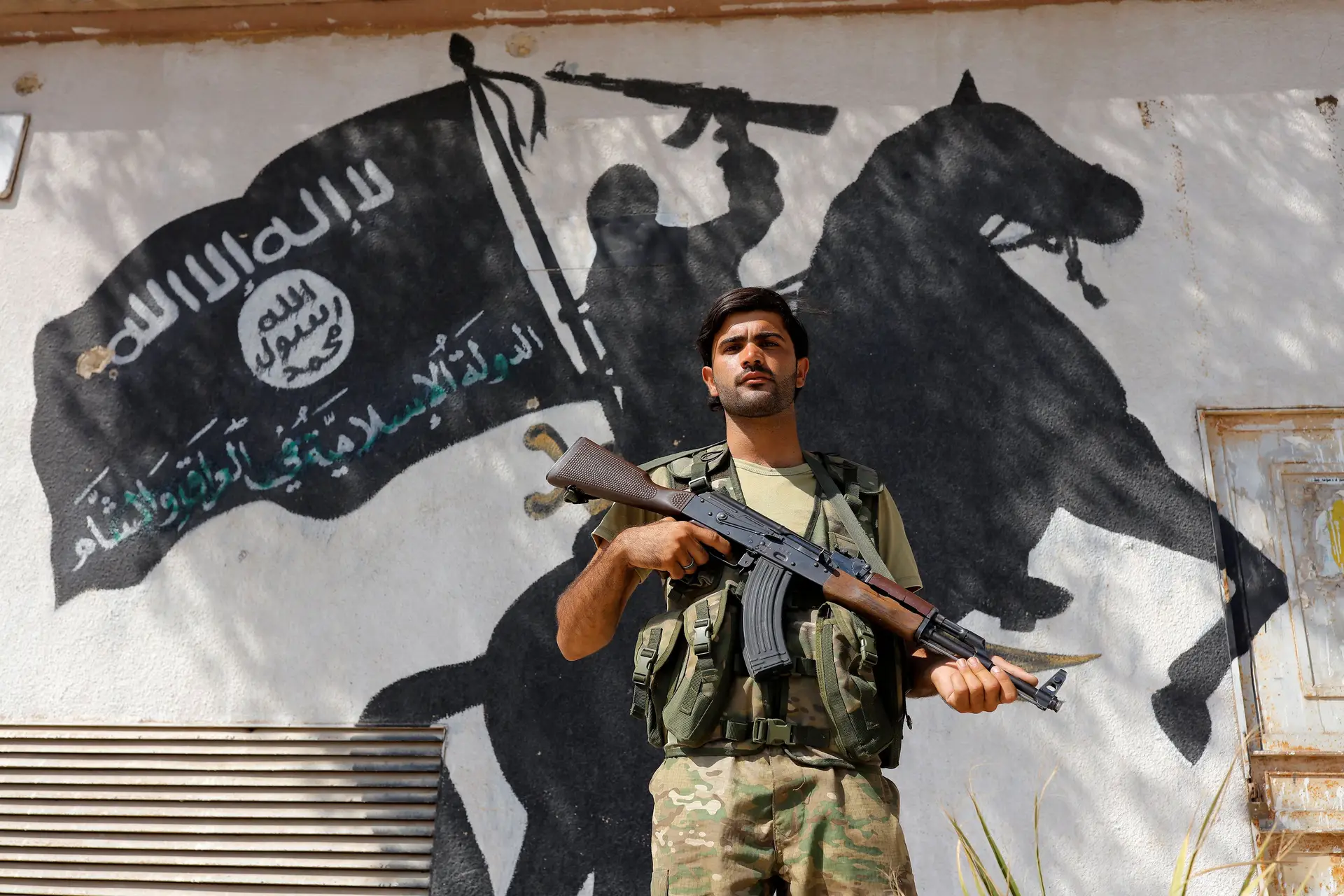 Militar do Exército de Libertação da Síria em frente a um mural do Daesh, Jarablus, Síria
