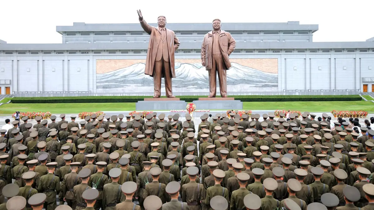 Exército da Coreia do Norte, civis, estudantes e crianças durante uma visita às estátuas de Kim II Sung e Kim Jong II, Coreia do Norte. 