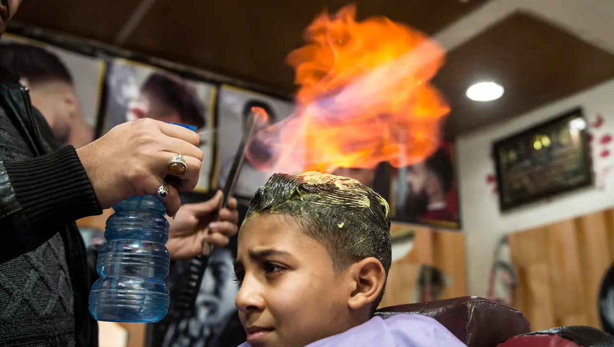 O barbeiro egípcio Hamada Ramadan usa fogo para alisar o cabelo de um cliente na sua loja em Gizé.