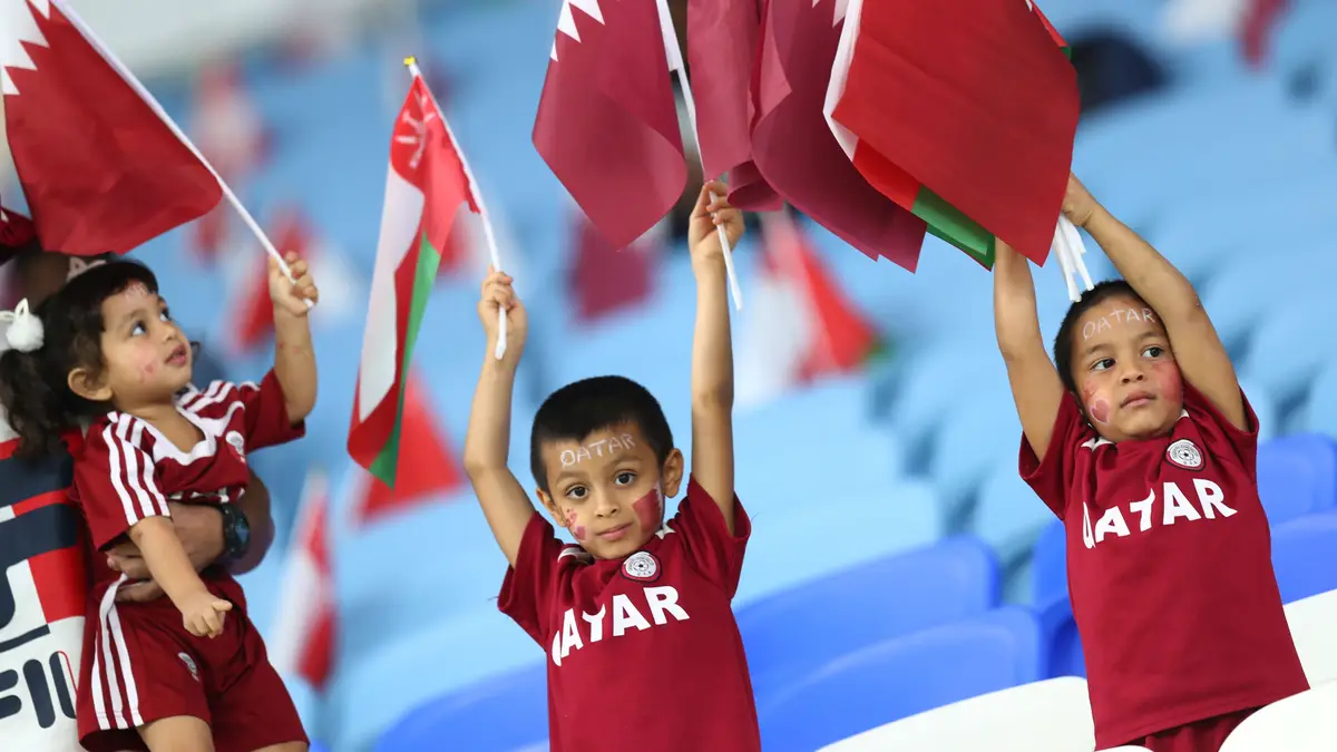 Crianças com as caras pintadas seguram bandeiras de Omã e do Qatar durante um jogo de qualificação para o Mundial de futebol de 2022, Qatar.