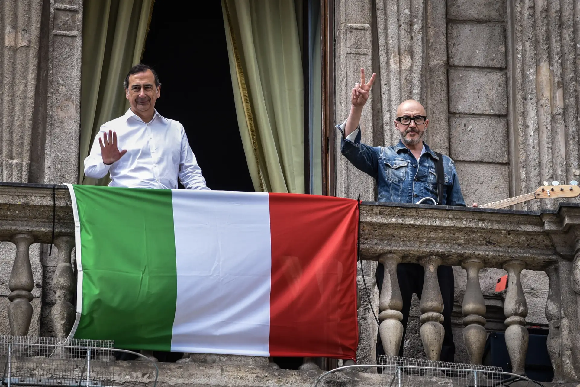 O político Giuseppe Sala e o músico italiano Saturnino gesticulam antes de cantar a popular canção 'Bella ciao' da varanda do Palazzo Marino, sobre a Piazza San Fedele, no centro de Milão, no norte da Itália.