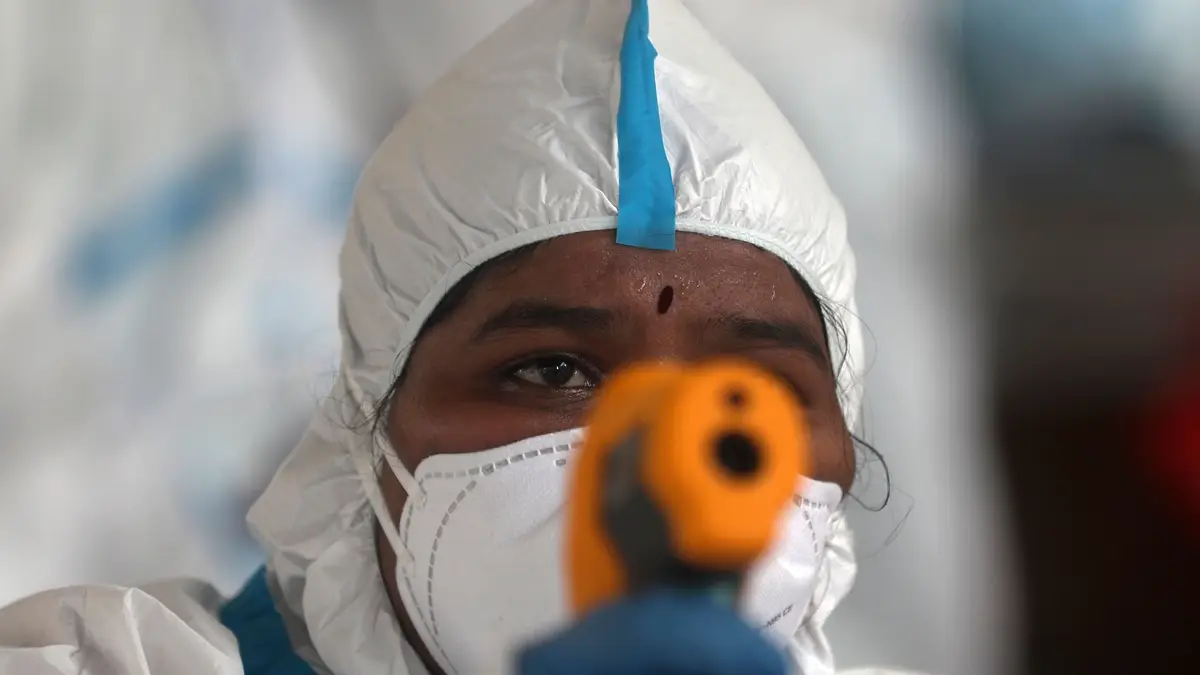 Um profissional de saúde mede a temperatura a uma mulher (ausente na imagem) em Dharavi, Índia